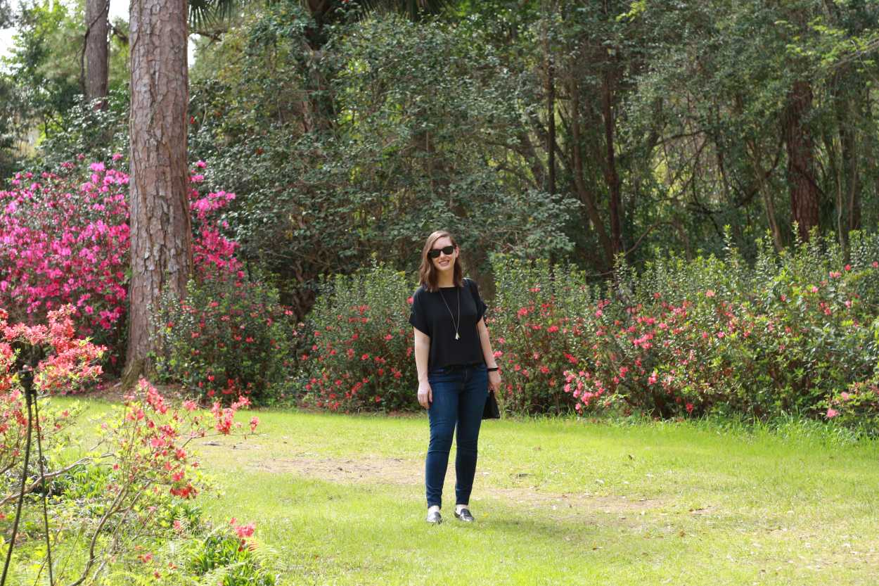 Alyssa wears a black silk tee with blue skinny jeans and stands in a garden