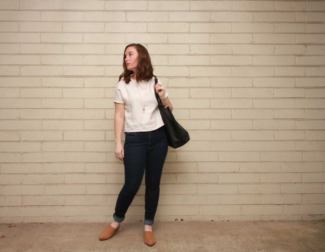 Alyssa wears a homemade white linen tee, skinny blue jeans, and nude mules and carries a tote bag