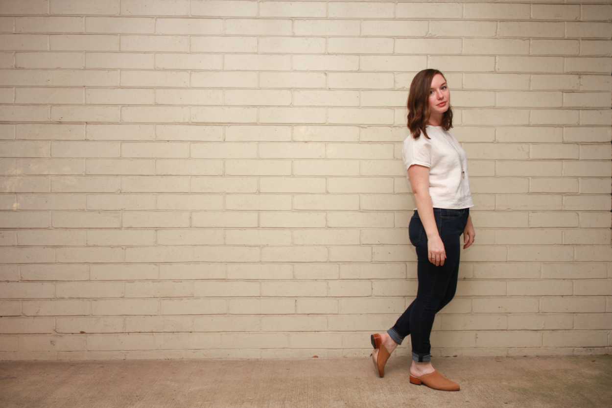 Alyssa wears a homemade white linen tee, skinny blue jeans, and nude mules and turns her body to the side