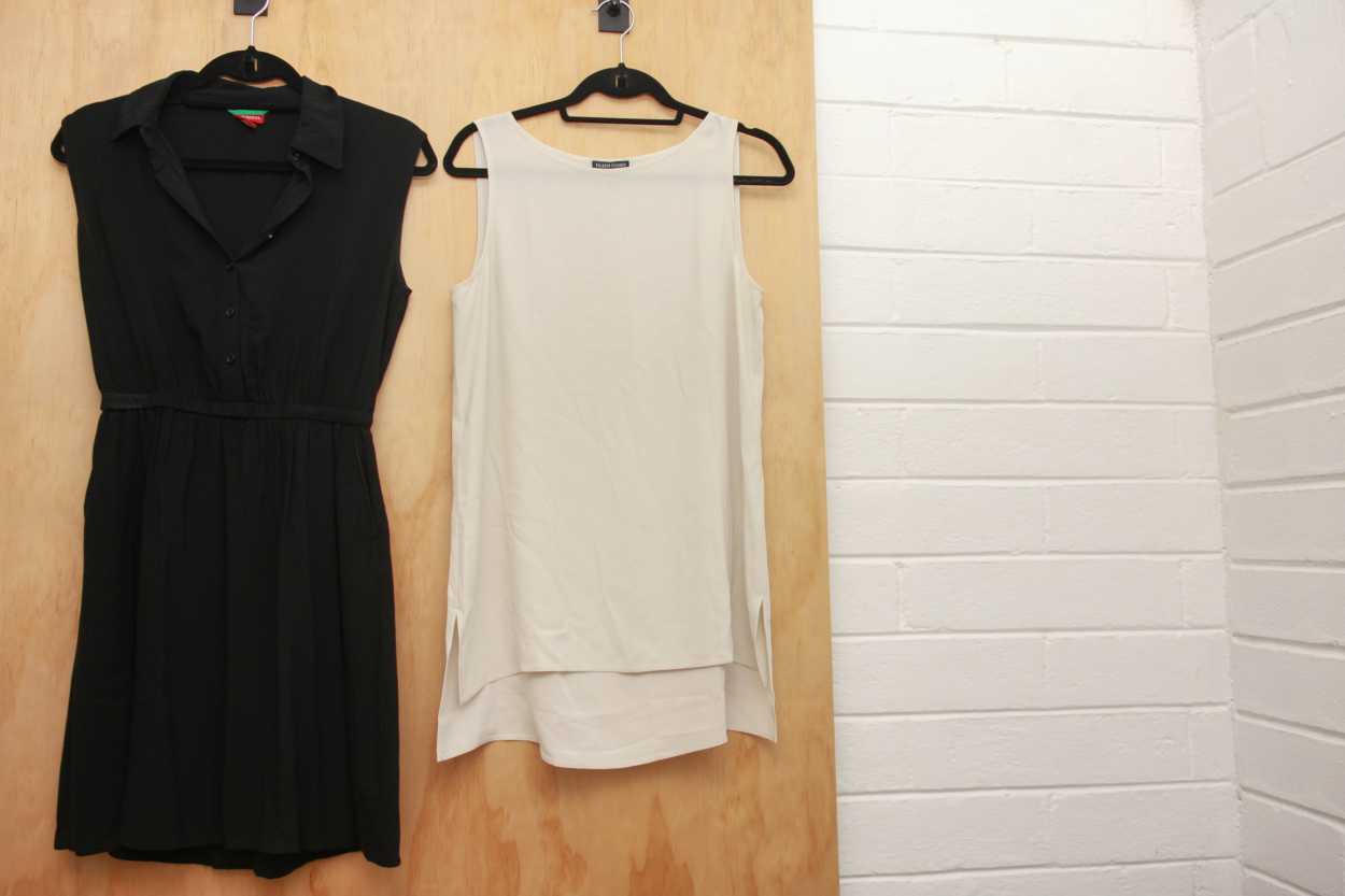 A black sleeveless dress and white tunic hang from a door