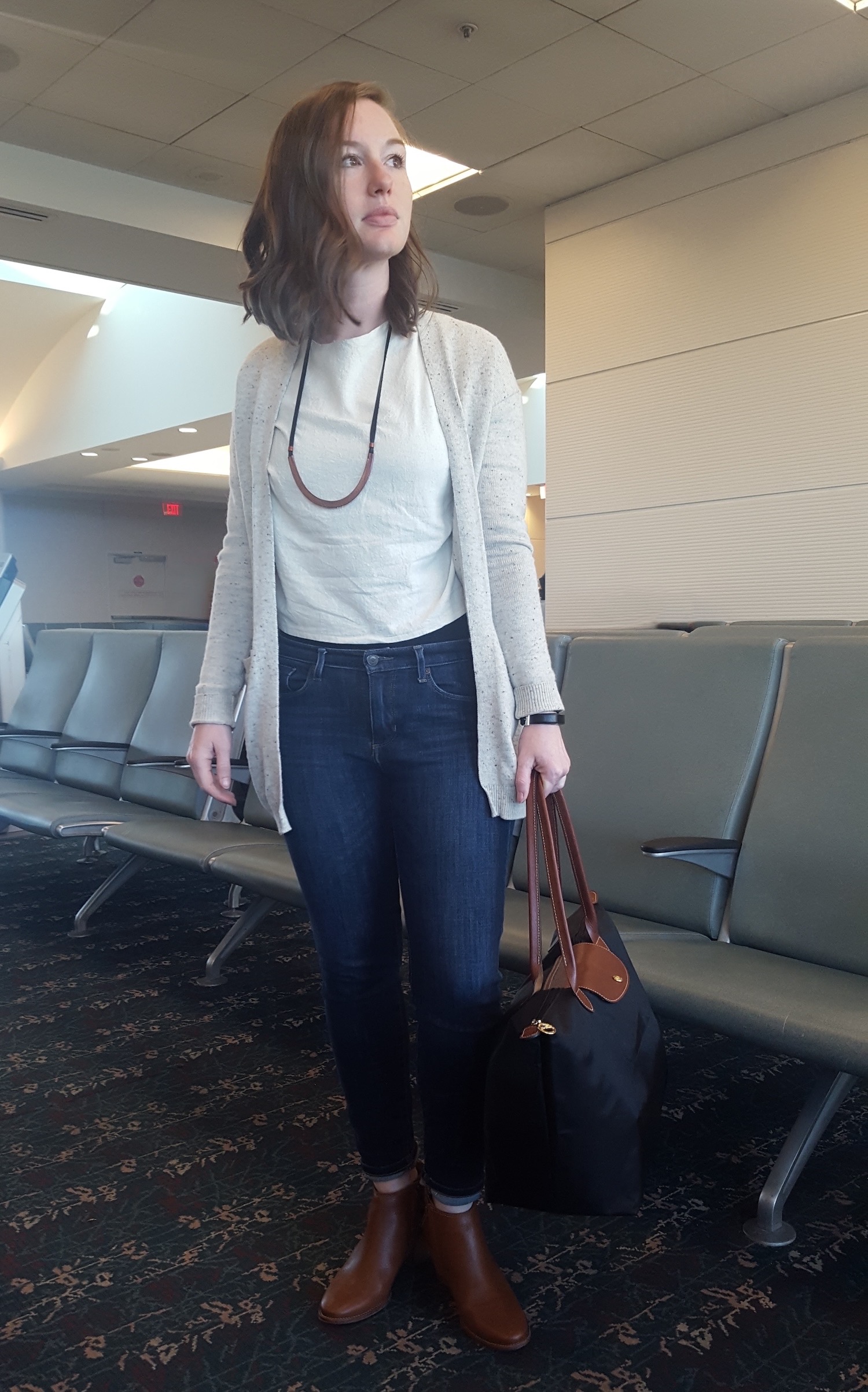 Alyssa wears jeans, boots, and a cardigan in the airport