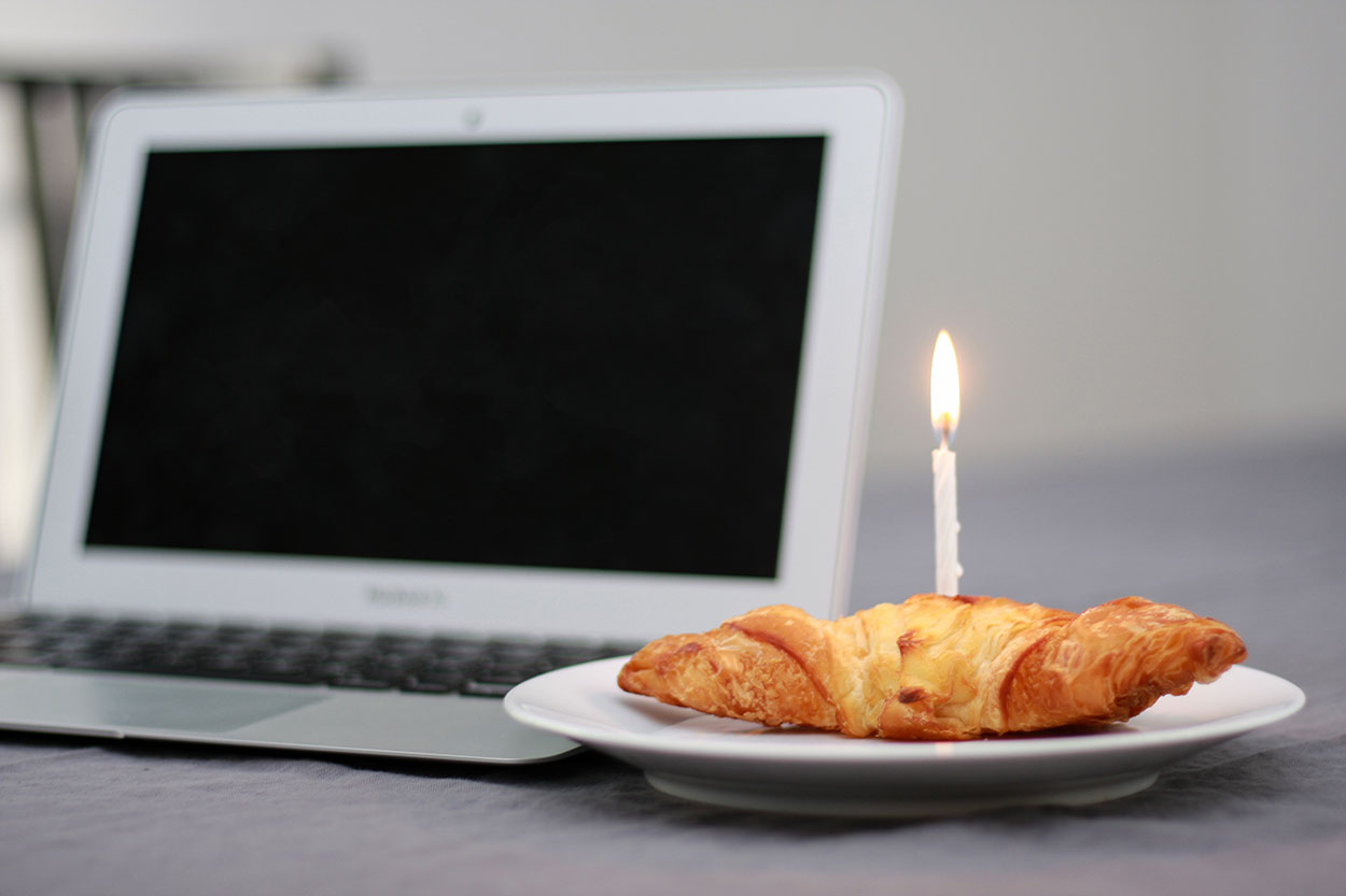 A croissant with a candle in it next to a laptop