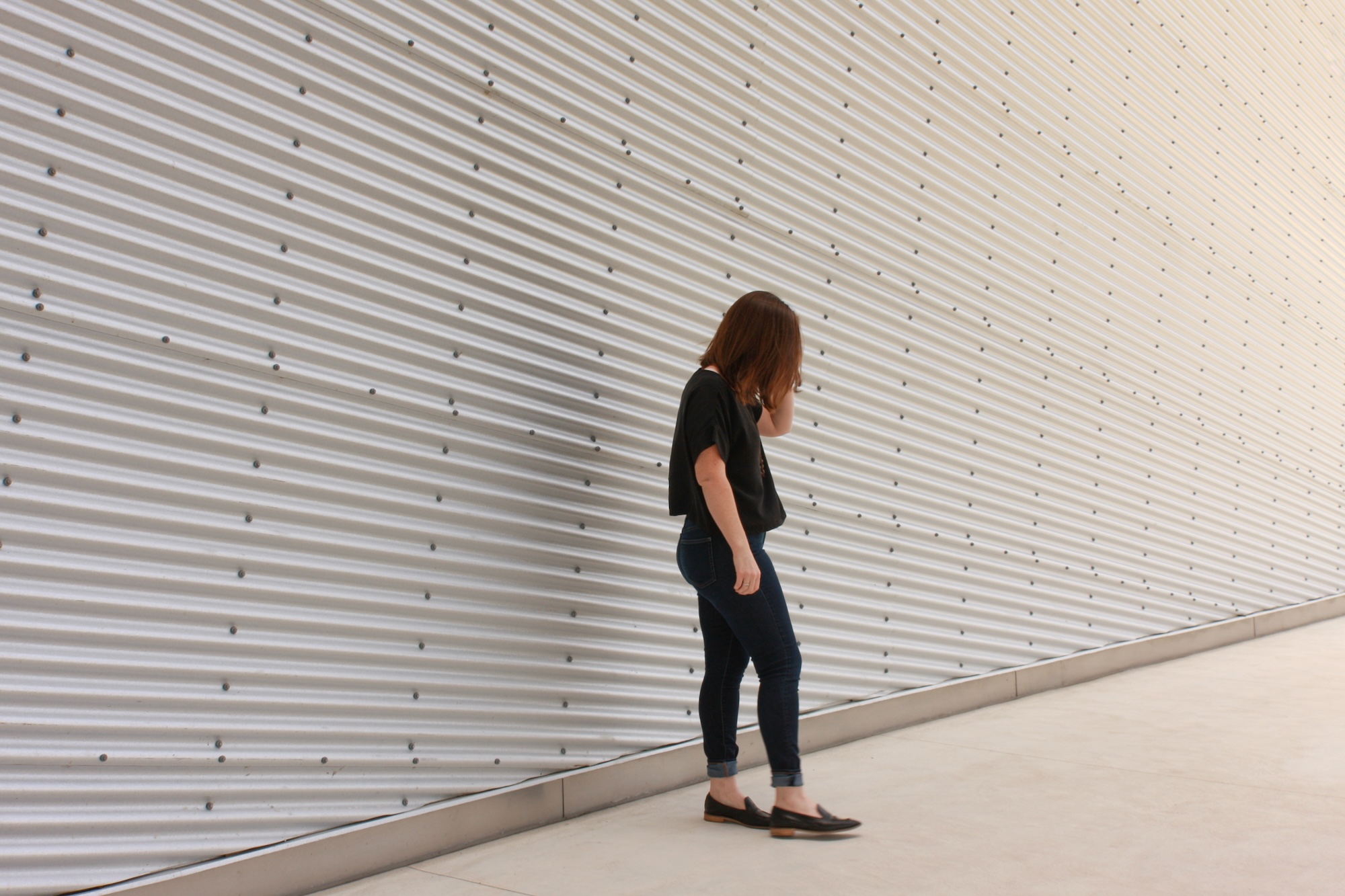 Alyssa wears a silk tee, blue jeans, and black mules while facing sideways to the camera