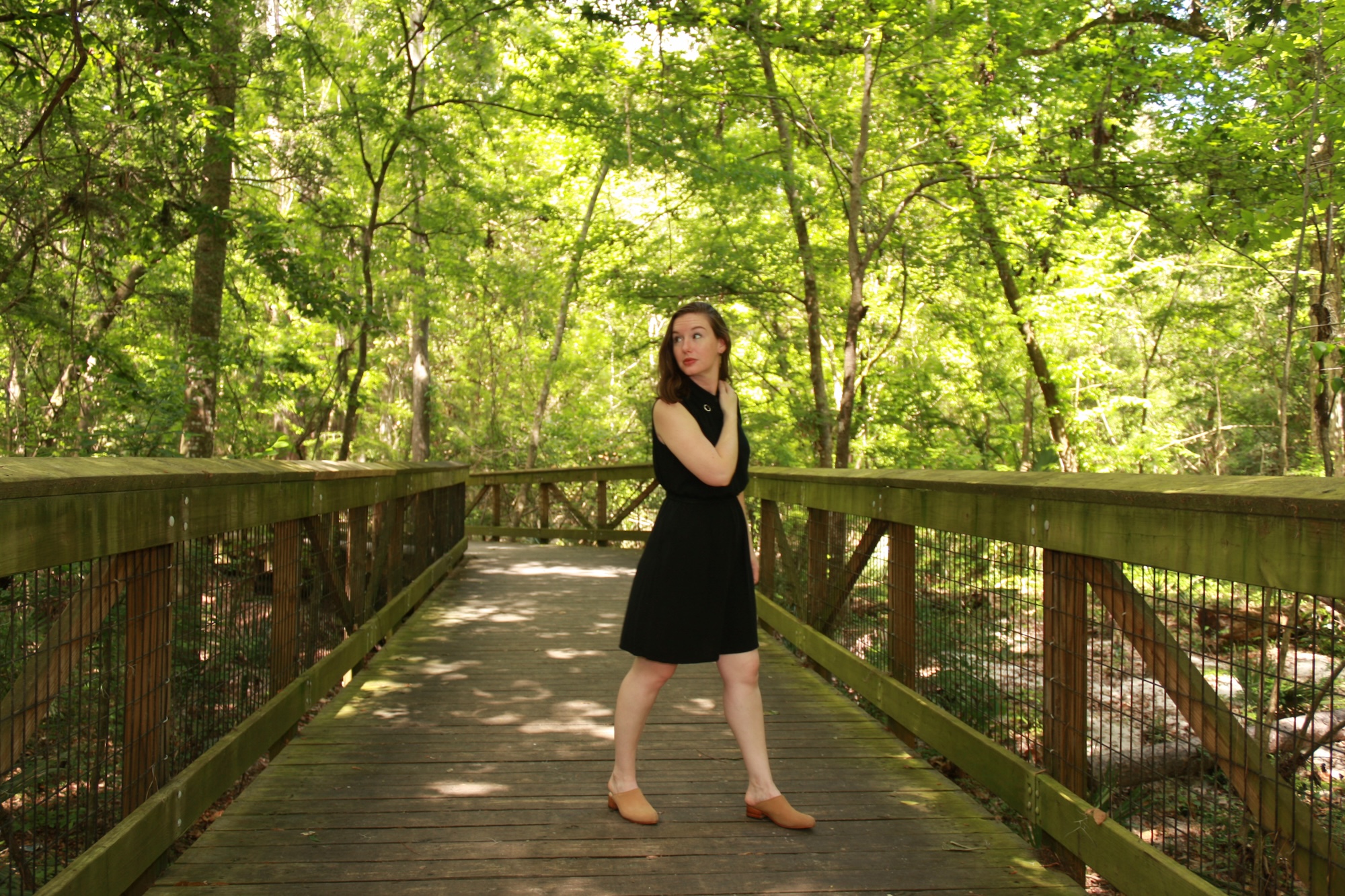 Alyssa wears a black shirtdress with nude mules on a bridge