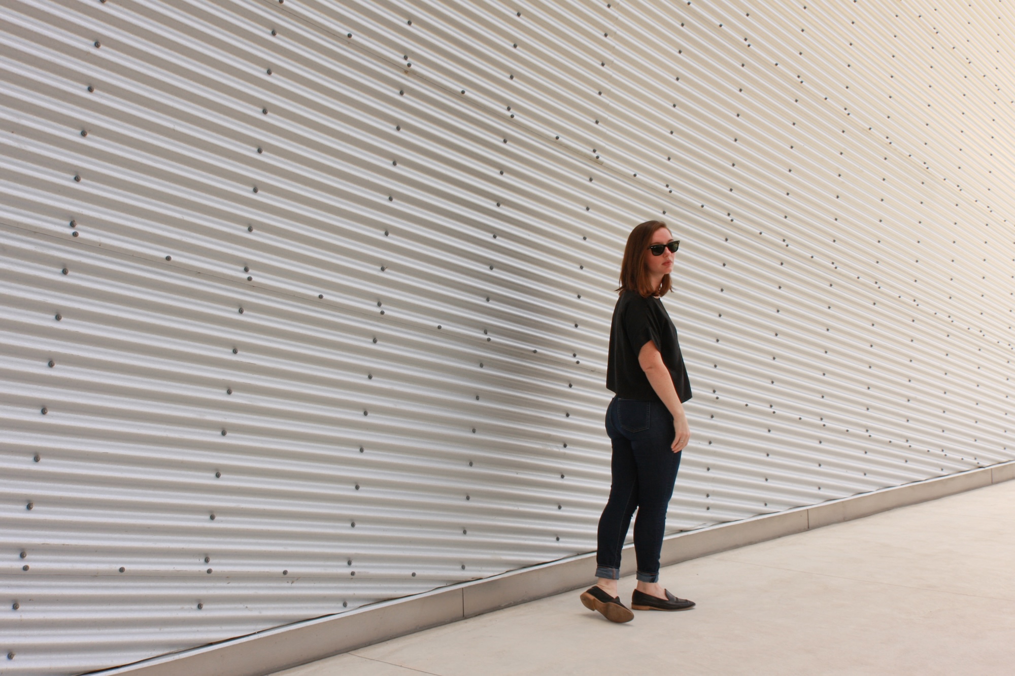 Alyssa wears a silk tee, blue jeans, and black mules while facing away from the camera