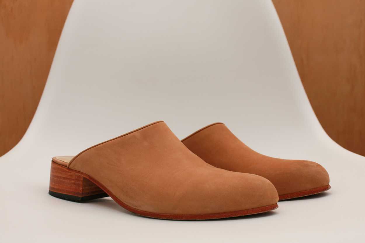 A pair of tan mules from Nisolo sit on a white chair