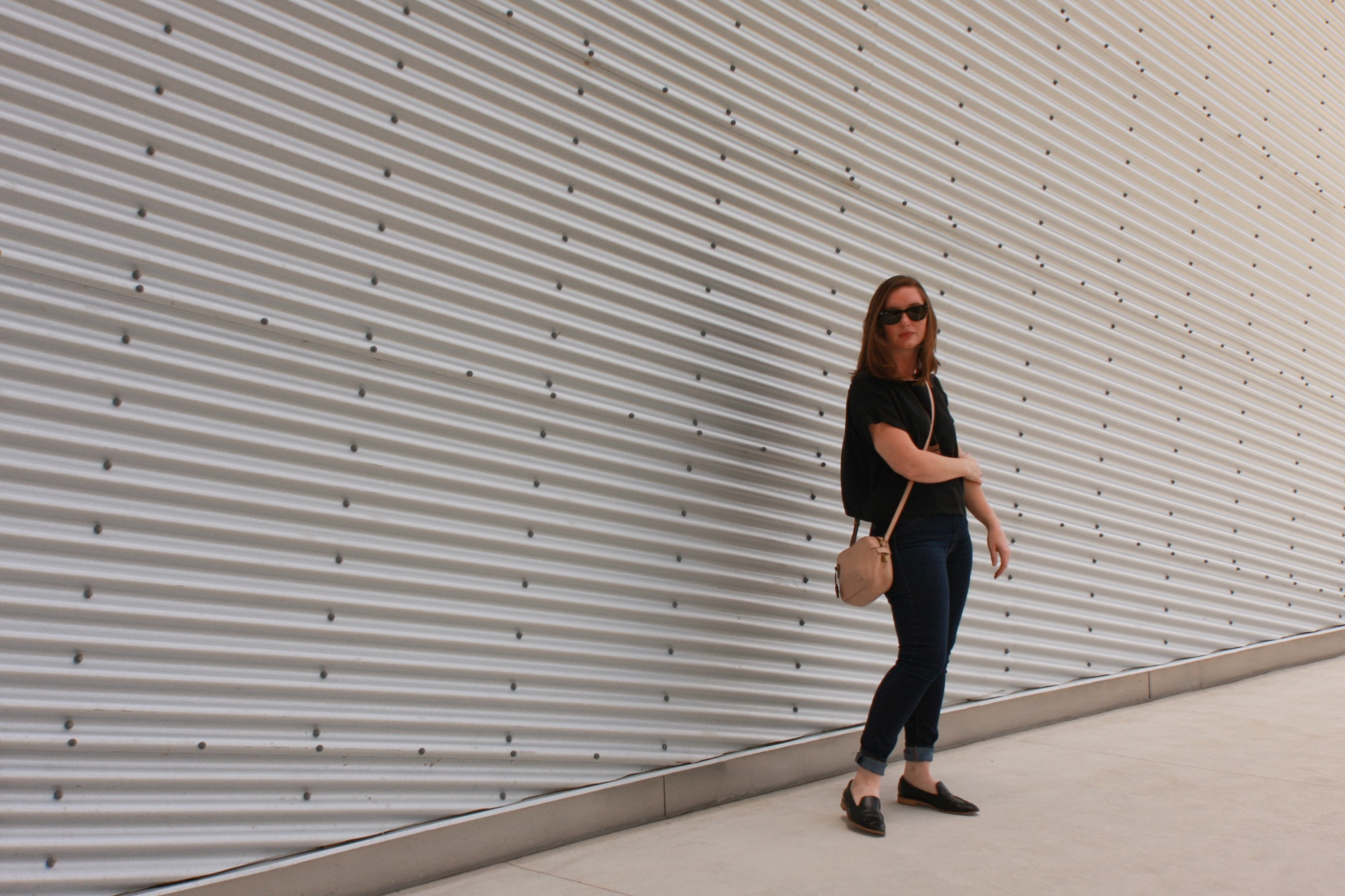 Alyssa wears a silk tee, blue jeans, and black mules with black sunglasses while turning sideways to the camera