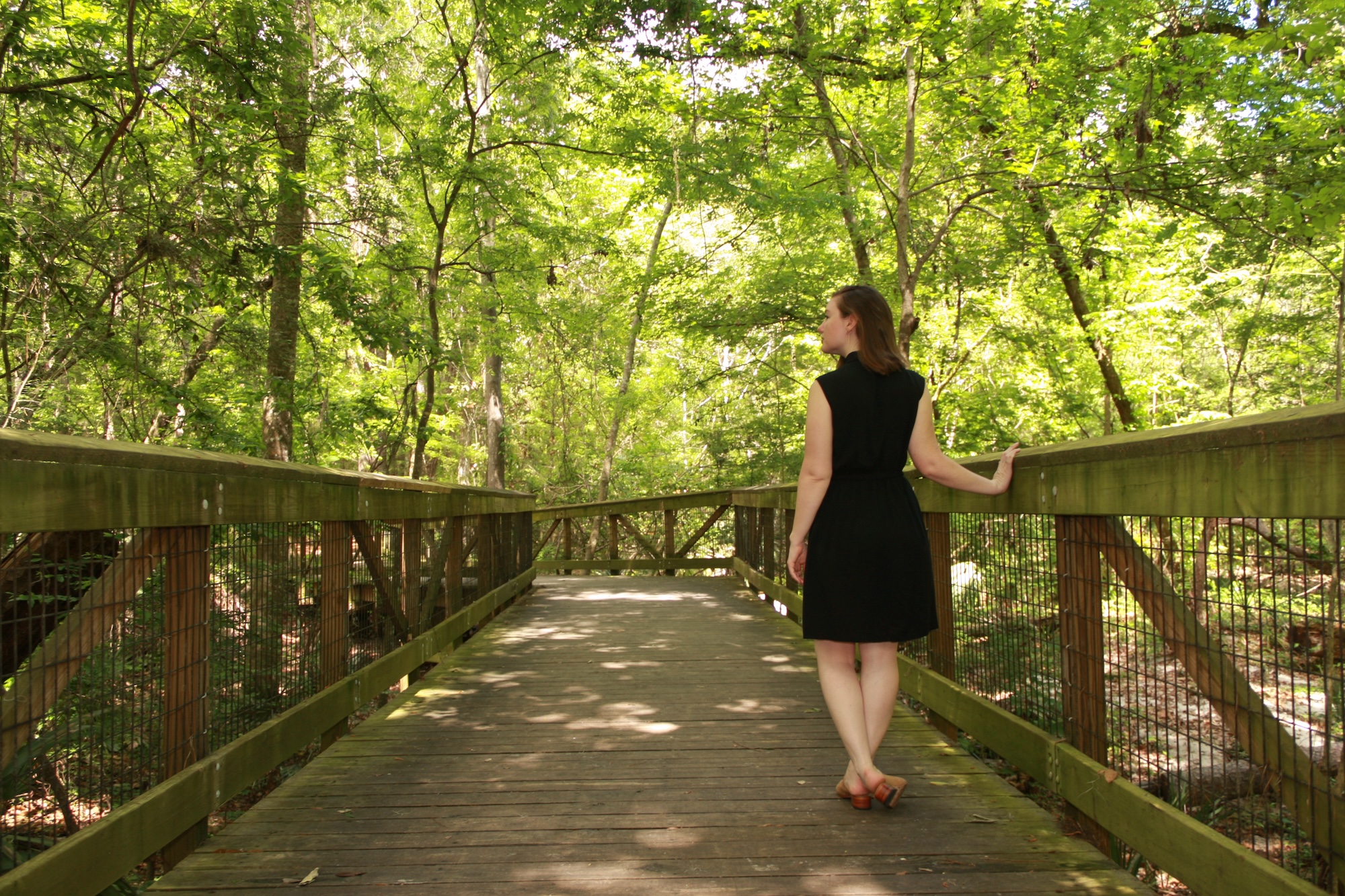 Alyssa wears a black shirtdress with nude mules and turns away from the camera