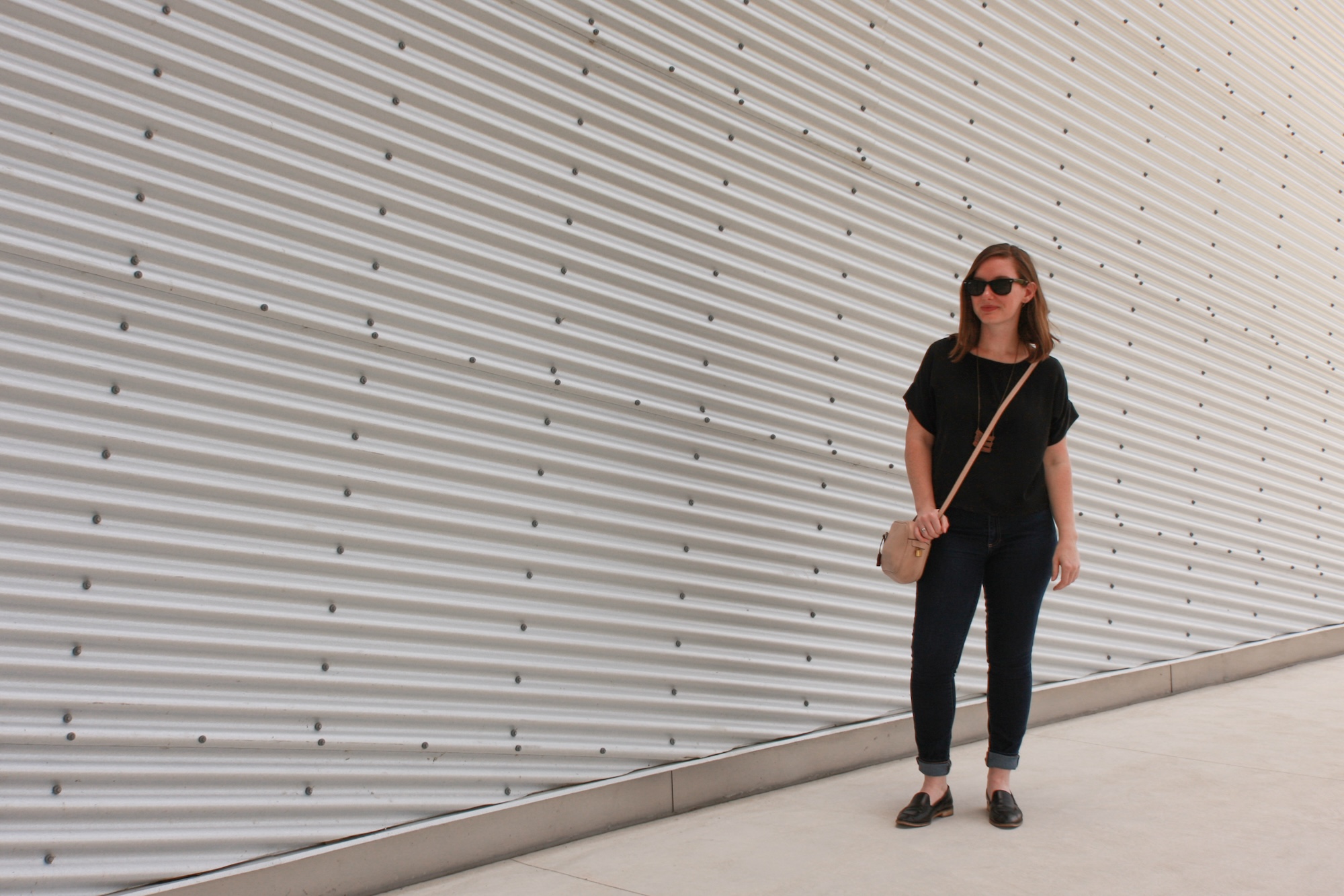 Alyssa wears a silk tee, blue jeans, and black mules with black sunglasses and a pink purse