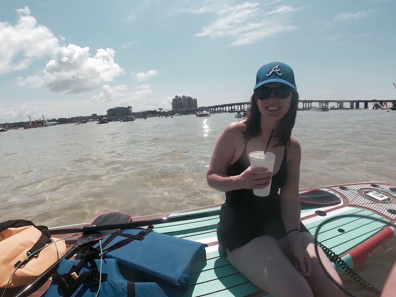 Alyssa sits on a paddleboard and drinks a daiquiri from a styrofoam cup