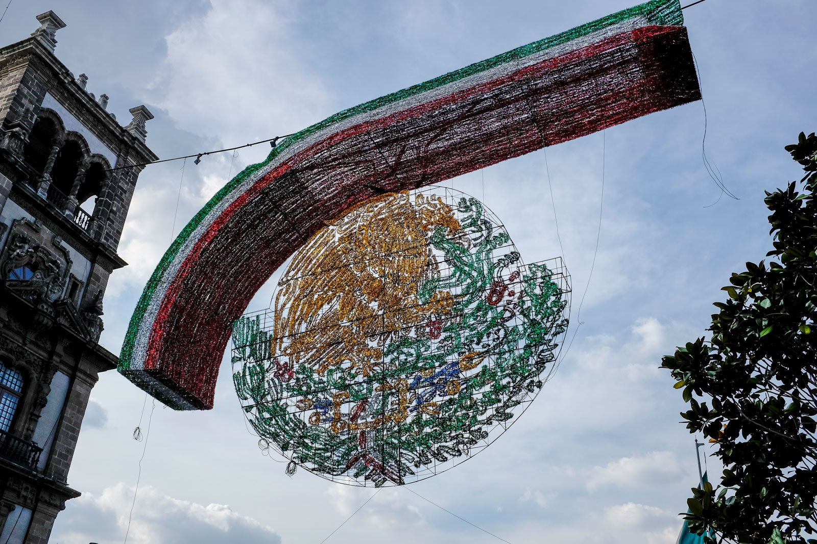A crafted emblem of the Mexico flag hangs over a street