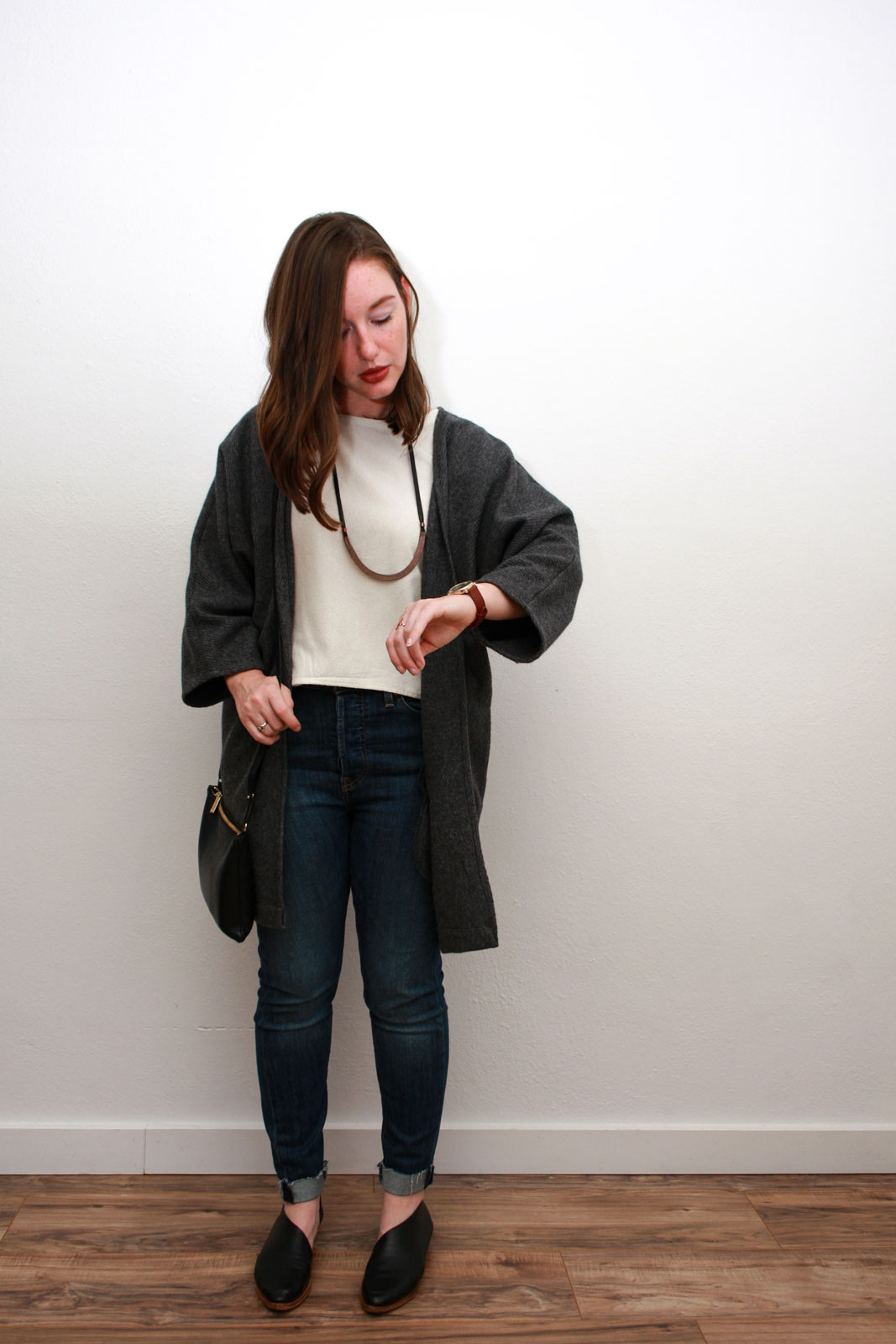 Alyssa wears a cream silk top, blue skinny jeans, grey cardigan and black asymmetrical flats while checking her watch