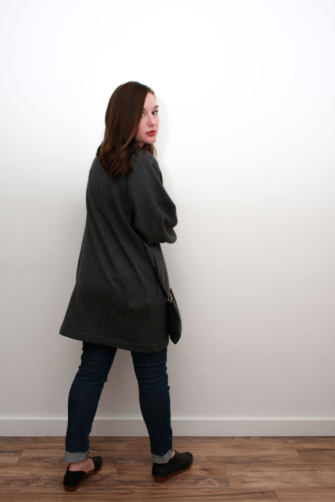 Alyssa wears a cream silk top, blue skinny jeans, grey cardigan and black asymmetrical flats while turning toward the camera