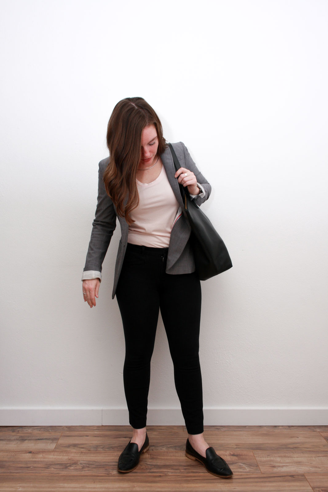 Alyssa wears a pink top, black pants, grey blazer, and carries a black tote
