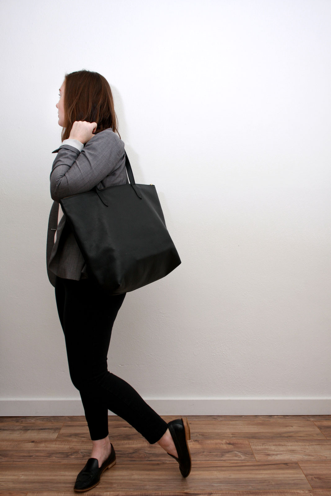 Alyssa wears a pink top, black pants, grey blazer, and carries a black tote while looking away from the camera