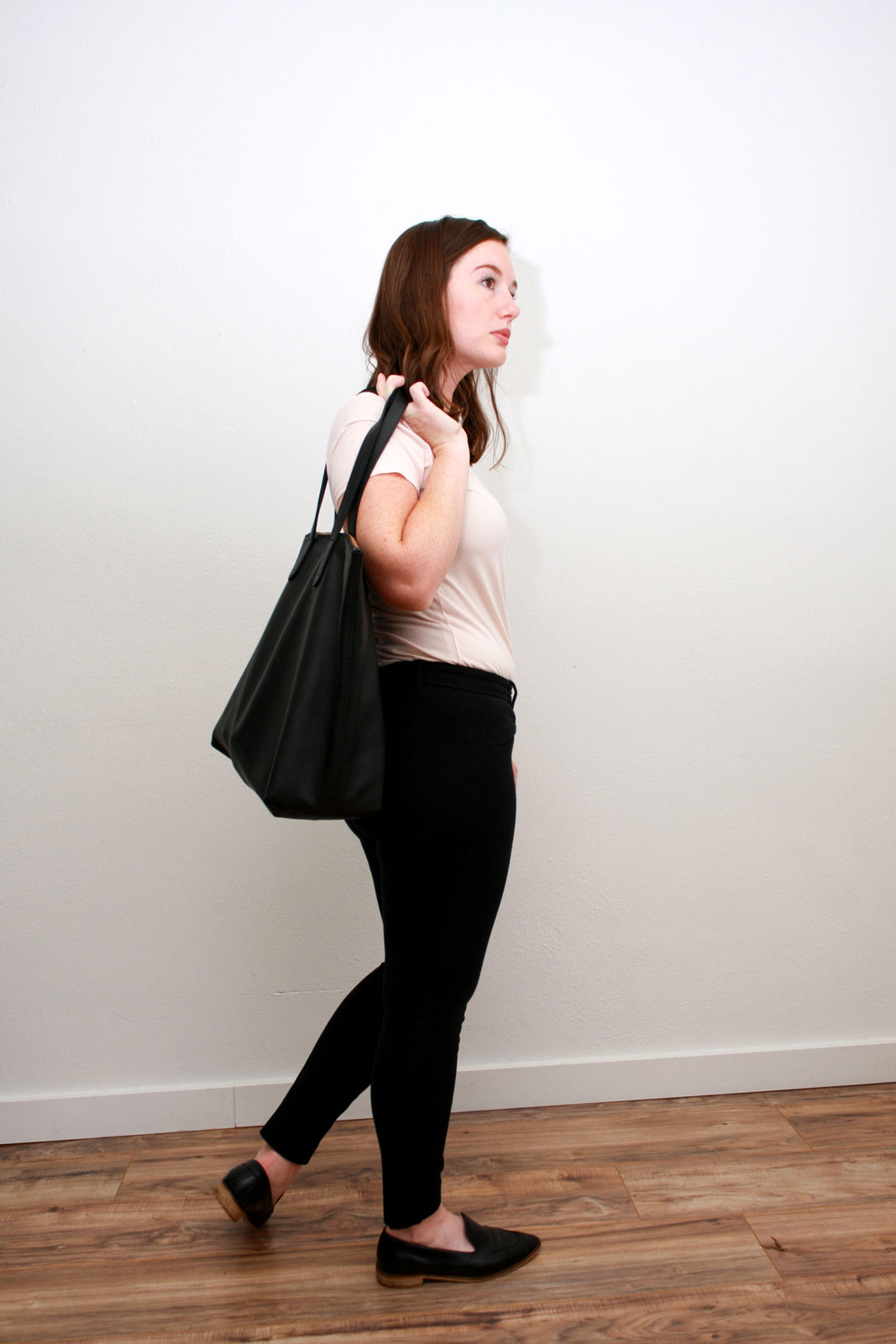 Alyssa wears a pink top, black pants, black loafers, and carries a black tote