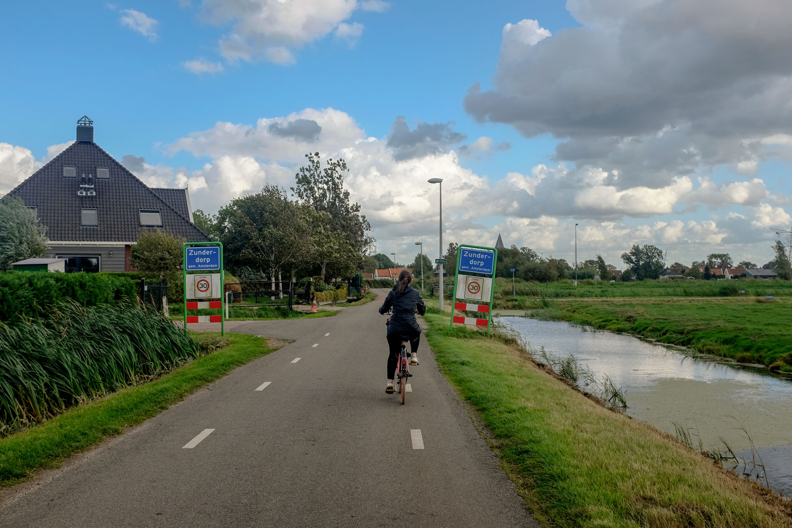 Alyssa bikes past a sign that reads Zunderdorp