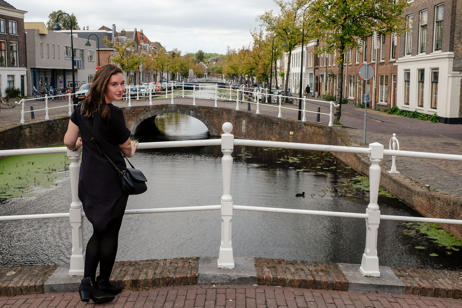 Alyssa stands in front of a Delft canal wearing a black dress, boots, and tights