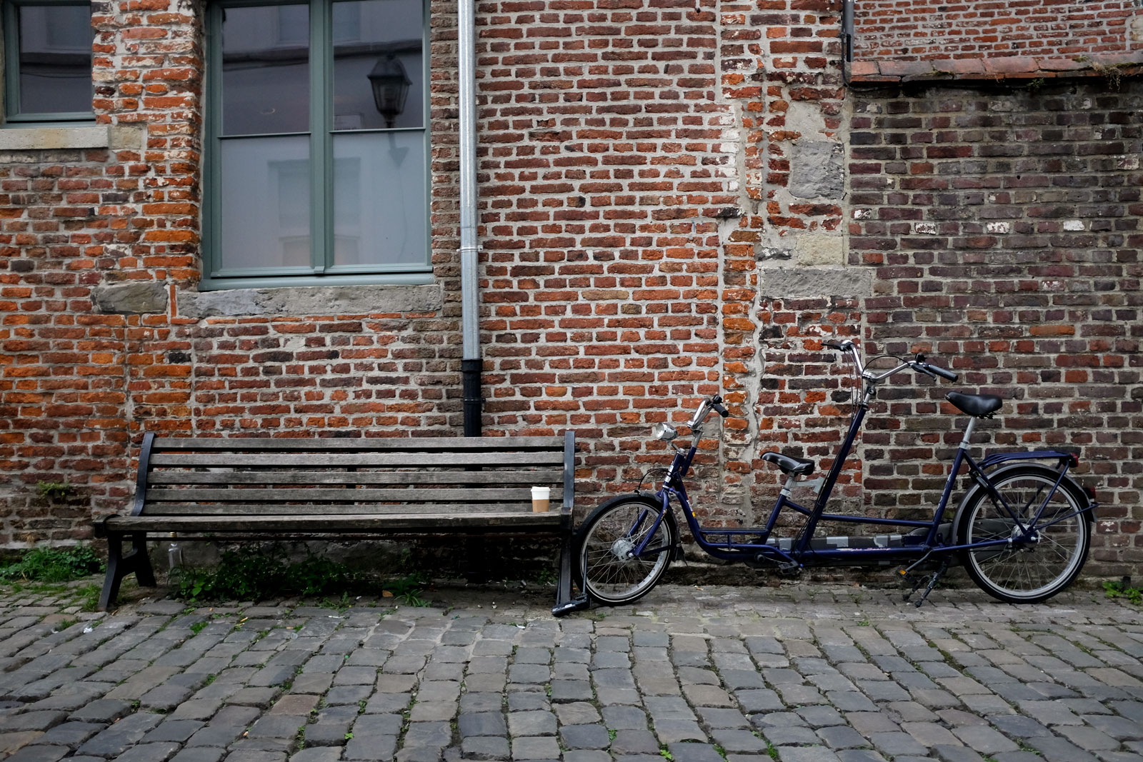 A tandem bike parked along a brick wall