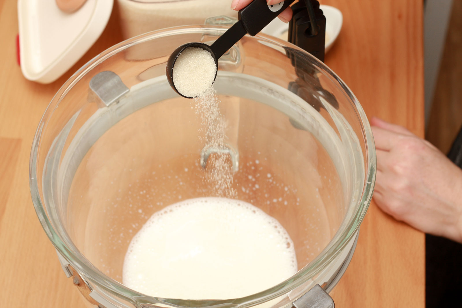 Alyssa pours granulated sugar into a bowl of warm milk
