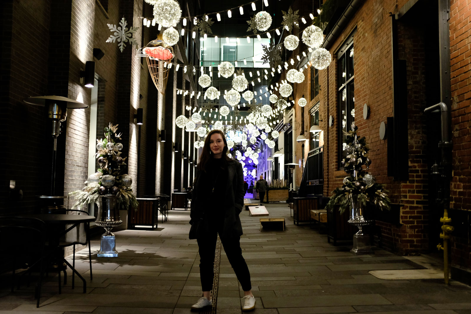 Alyssa stands in an alleyway lit with lights in Denver