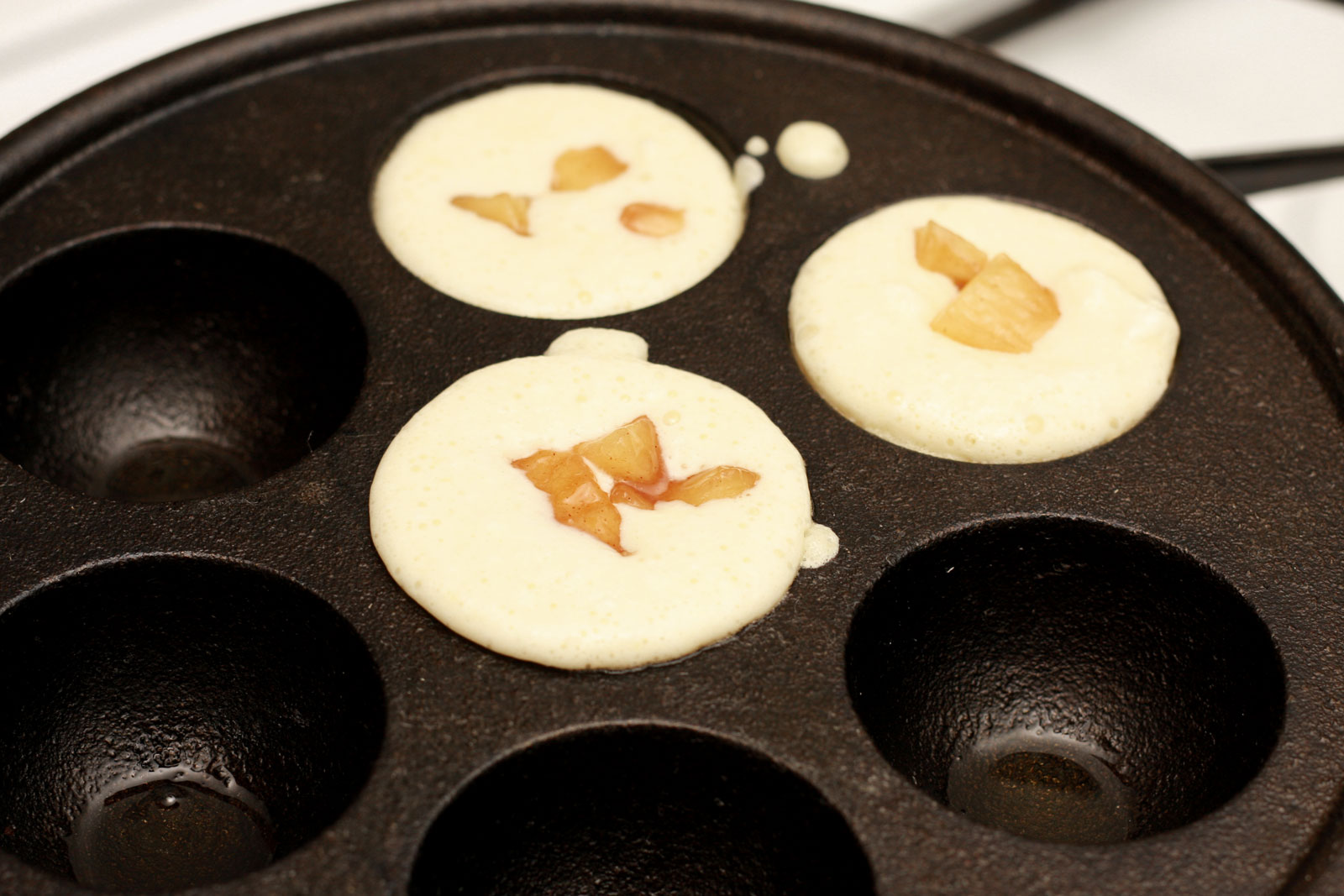three aebleskiver in a pan with apples