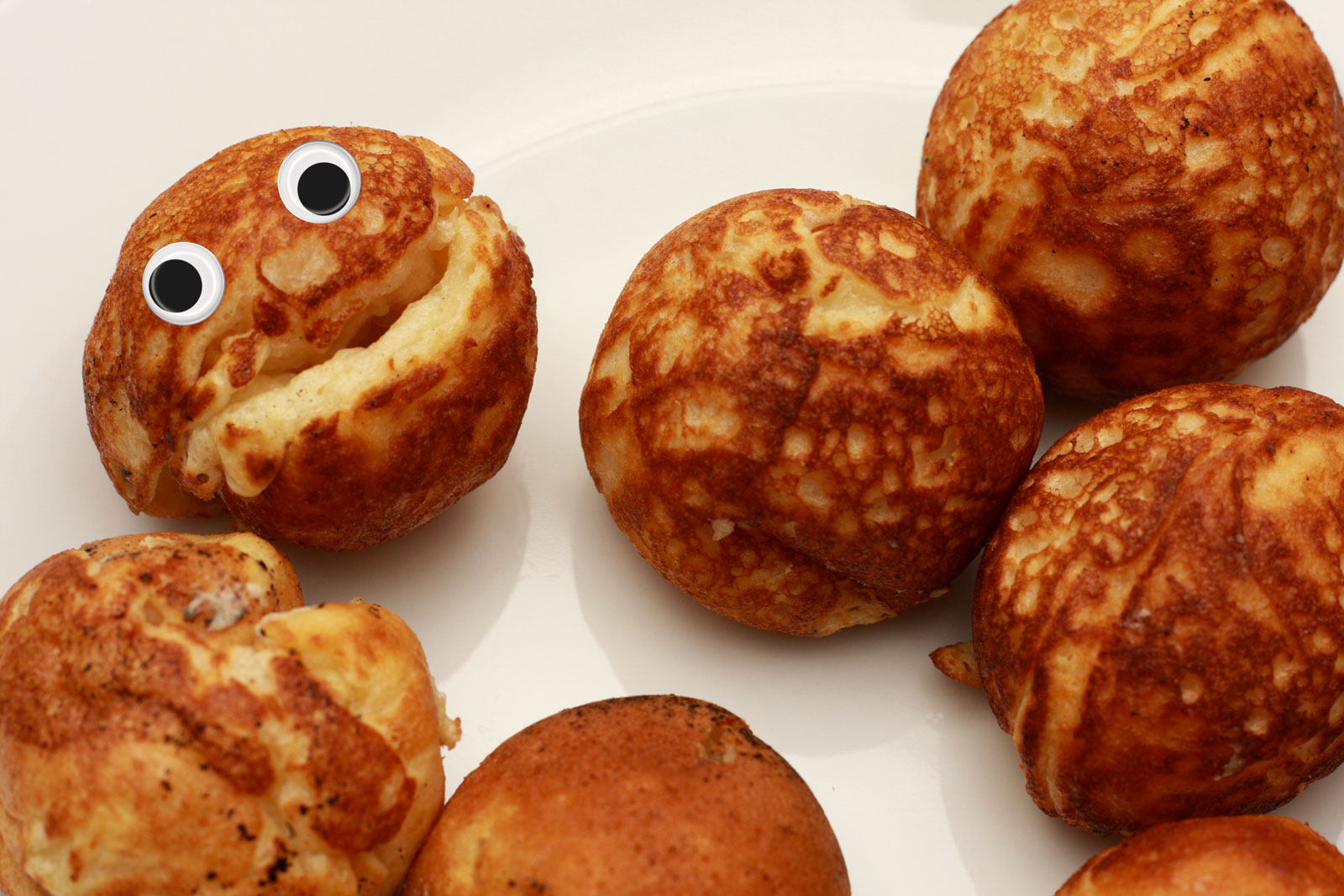 A plate of Æbleskiver, but one aebleskive has googly eyes