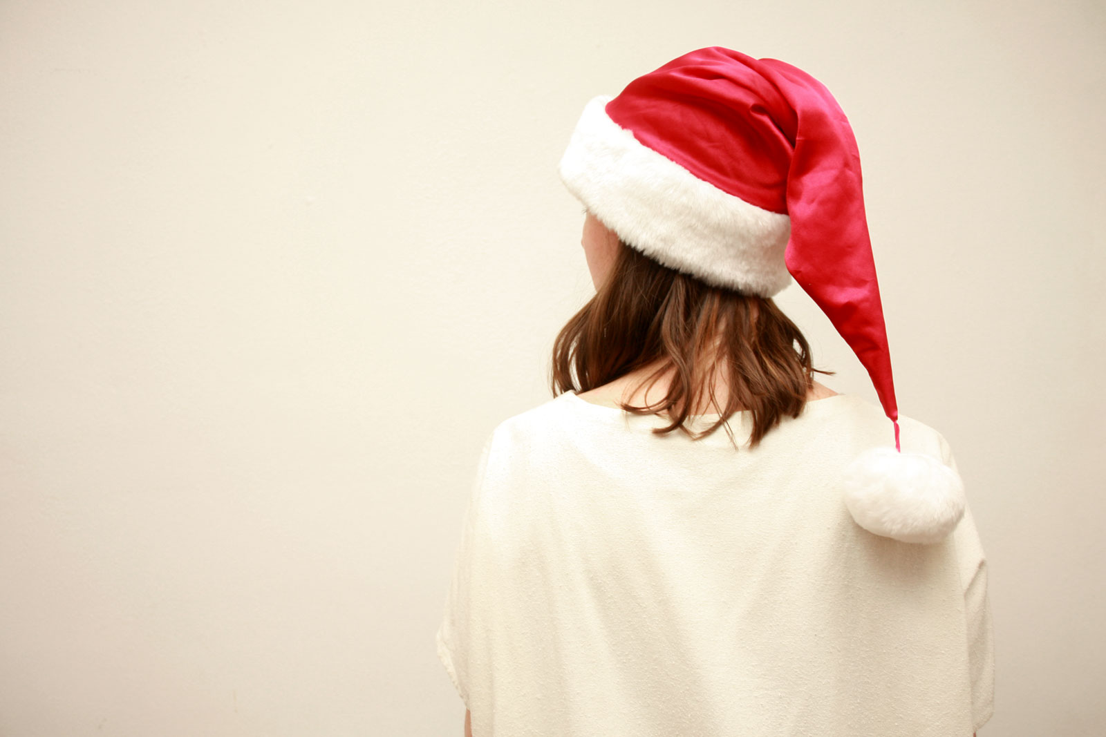 Alyssa wears a white top and a red Santa hat while facing away from the camera