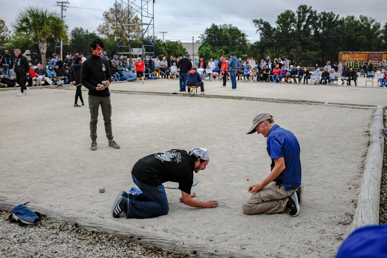 The umpire observes players measuring their throws in petanque
