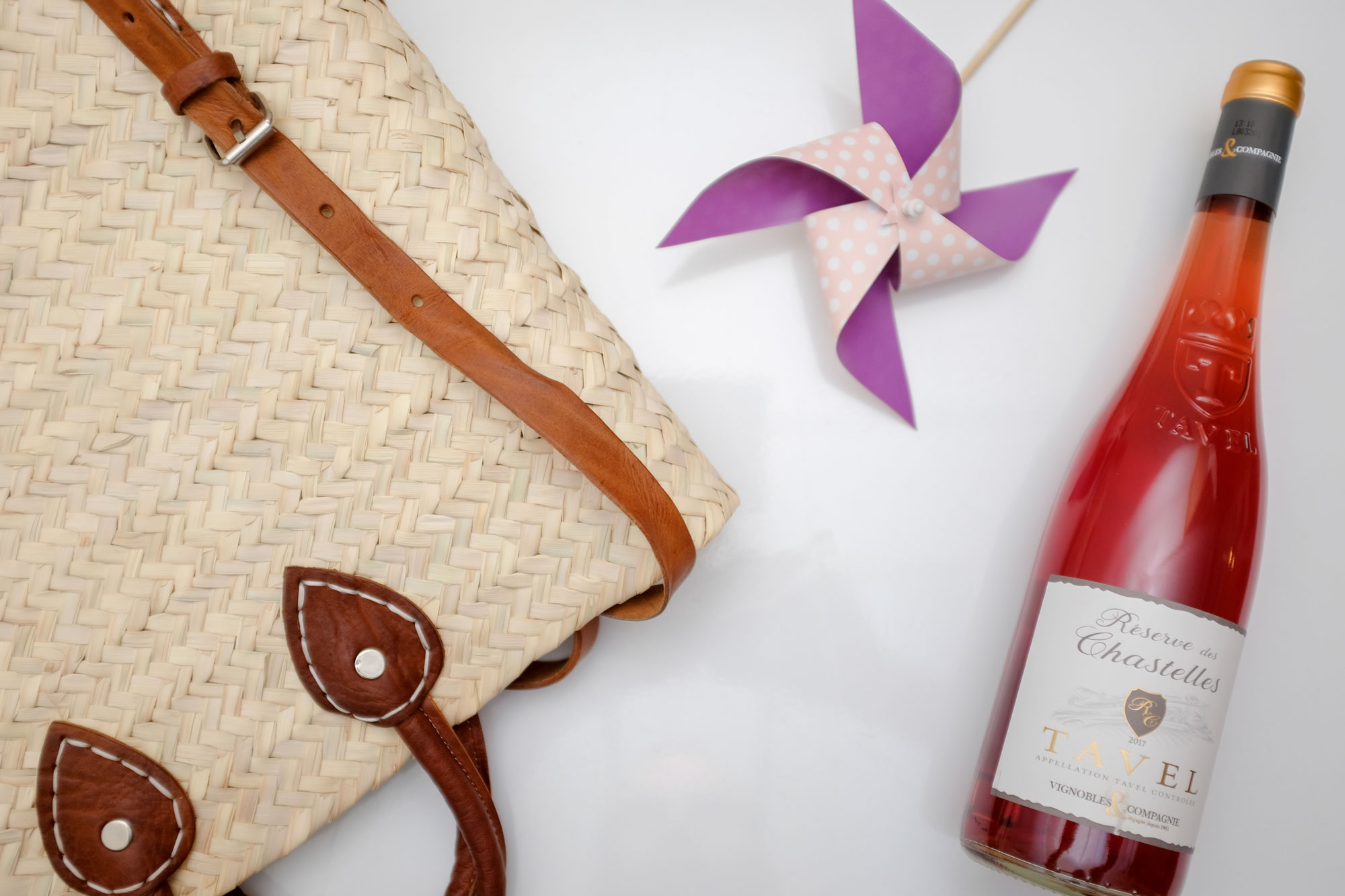 Woven bag, pinwheel, and bottle of rose wine laid flat