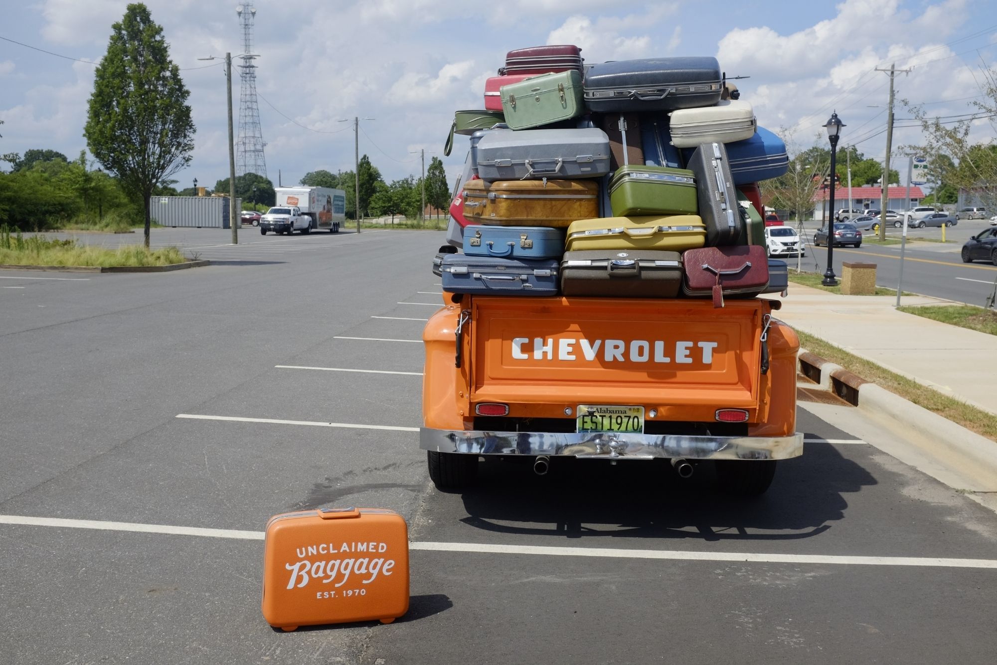 An orange vintage Chevy with a large mountain of suitcases in the bed