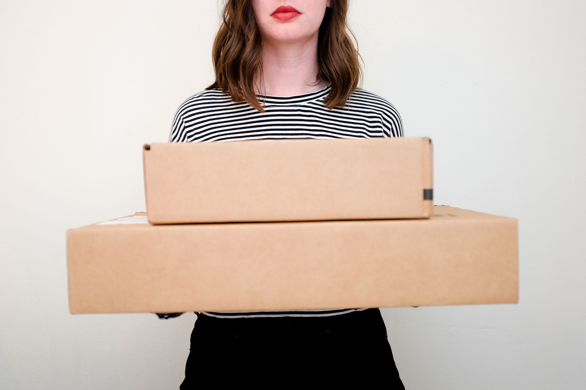 Alyssa wears a stripe tee and holds two mailer boxes