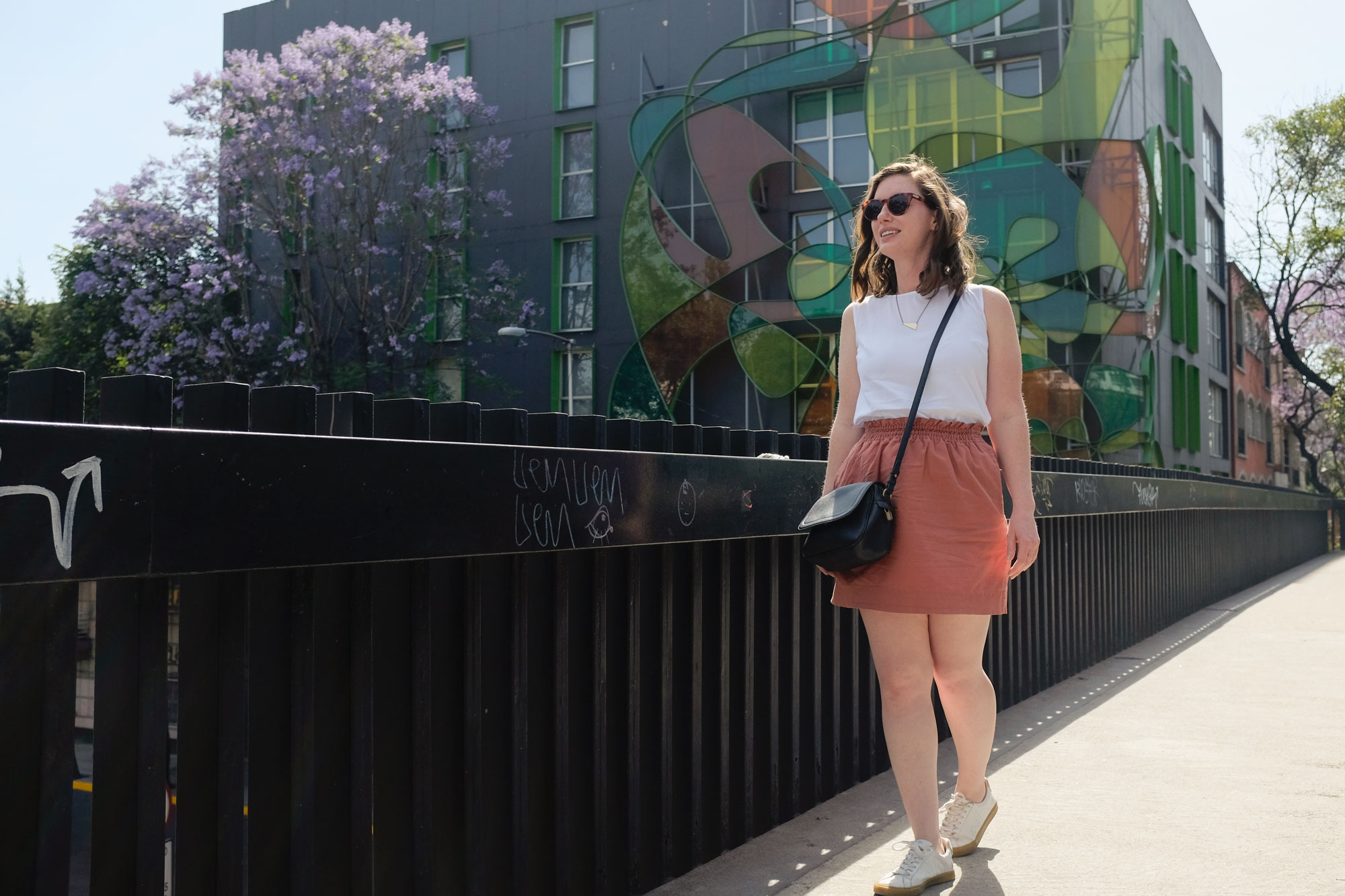 Alyssa walking on a bridge overpass with a white tank, rust skirt, and white sneakers