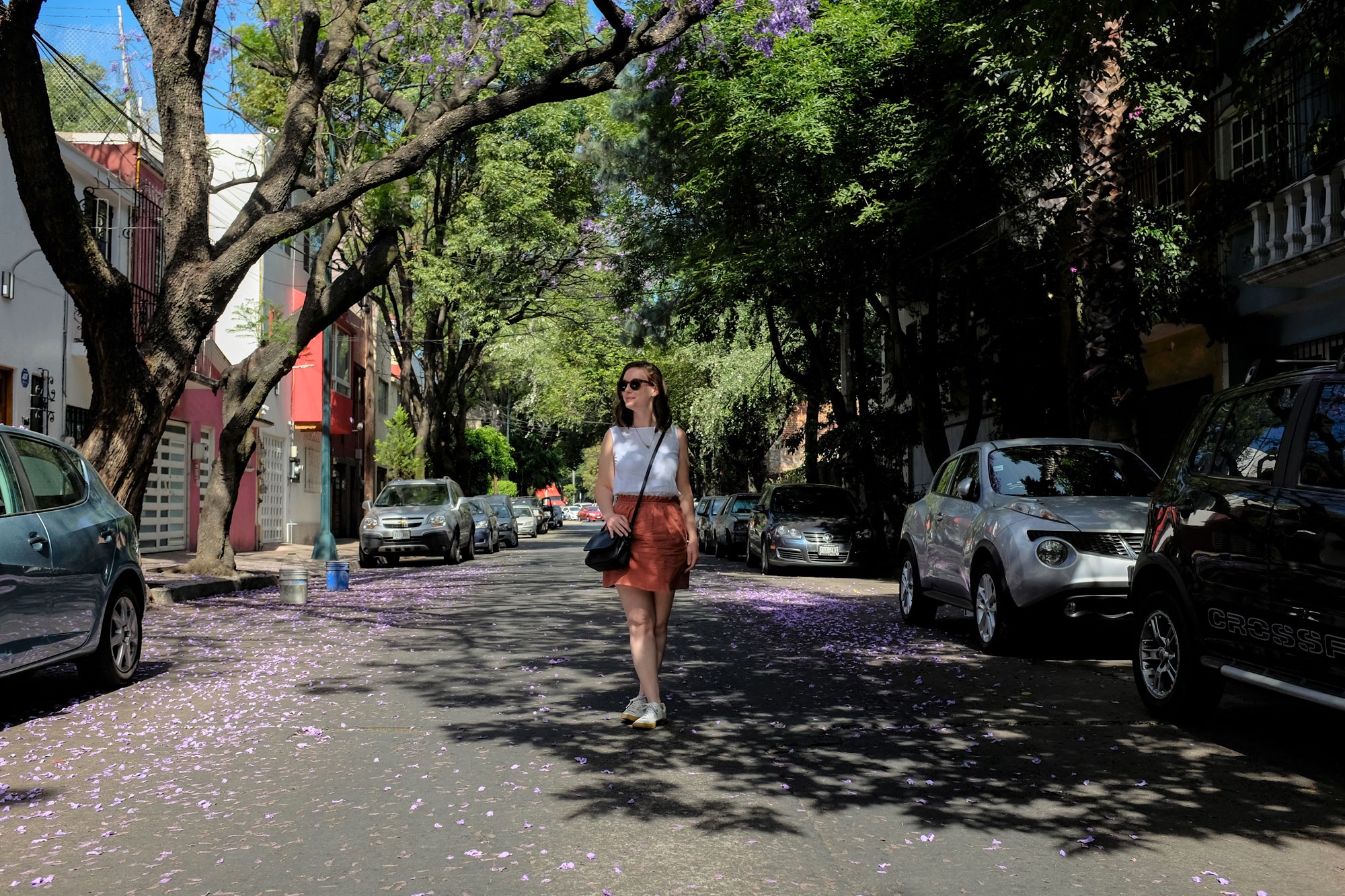 Alyssa walking down a street in mexico city wearing a white tank, rust skirt, and white sneakers