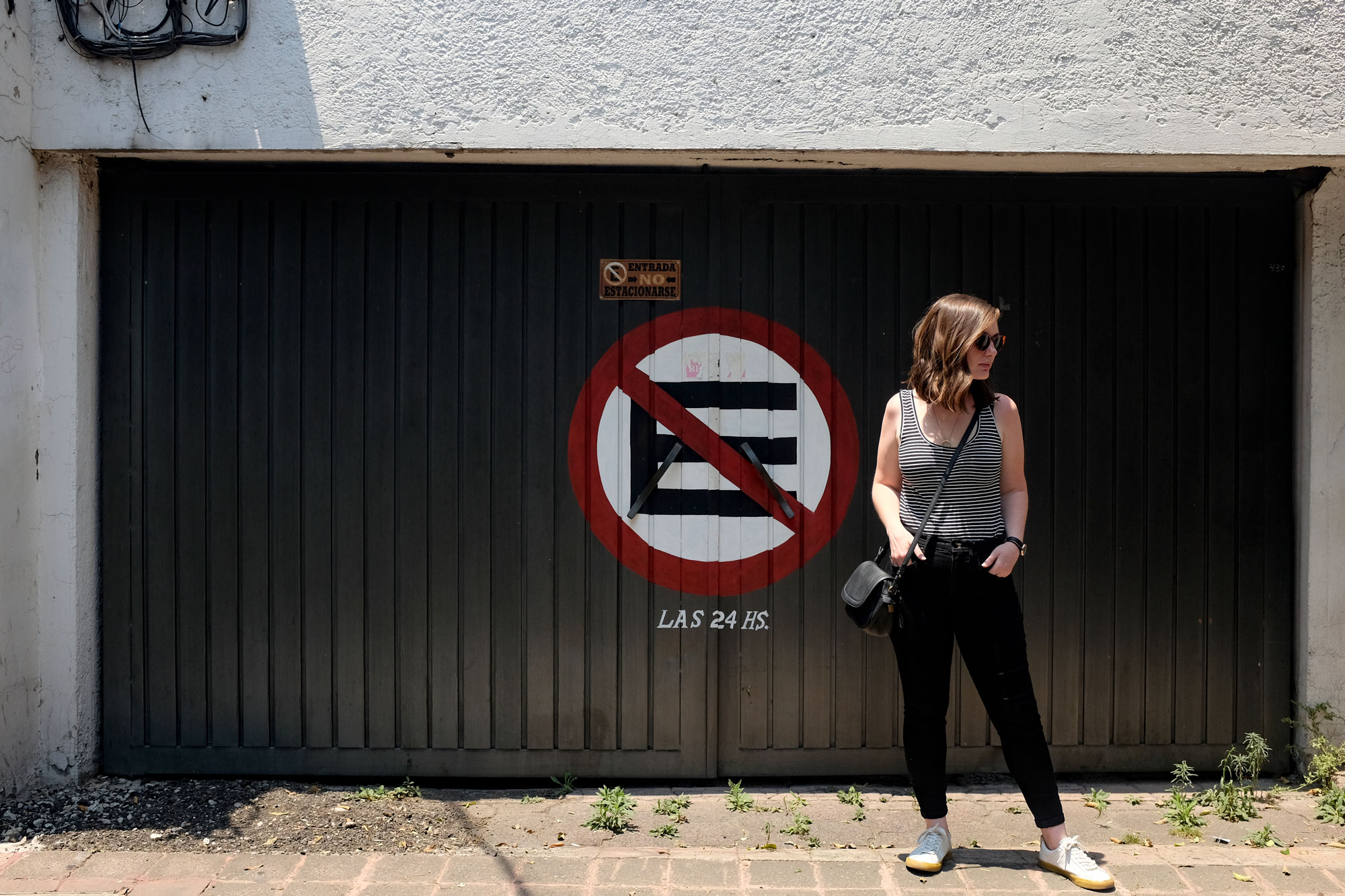 Alyssa standing in front of a sign that says no parking in spanish wearing black and white tank, black jeans, and white sneakers