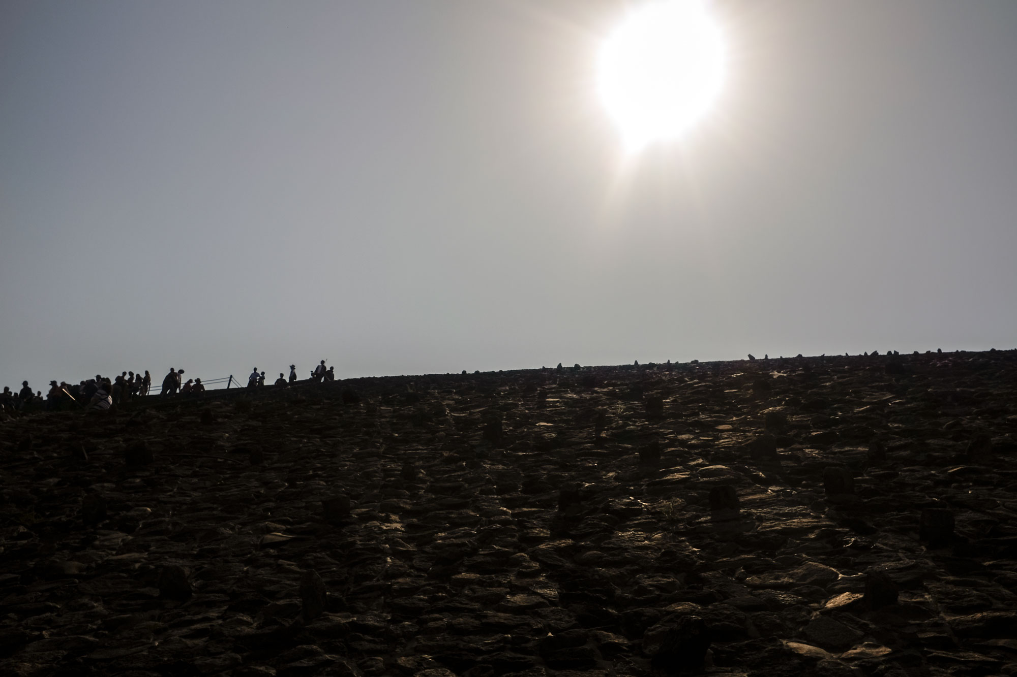 View up the pyramid of the sun with the sun overhead and the silhouettes of the people on top