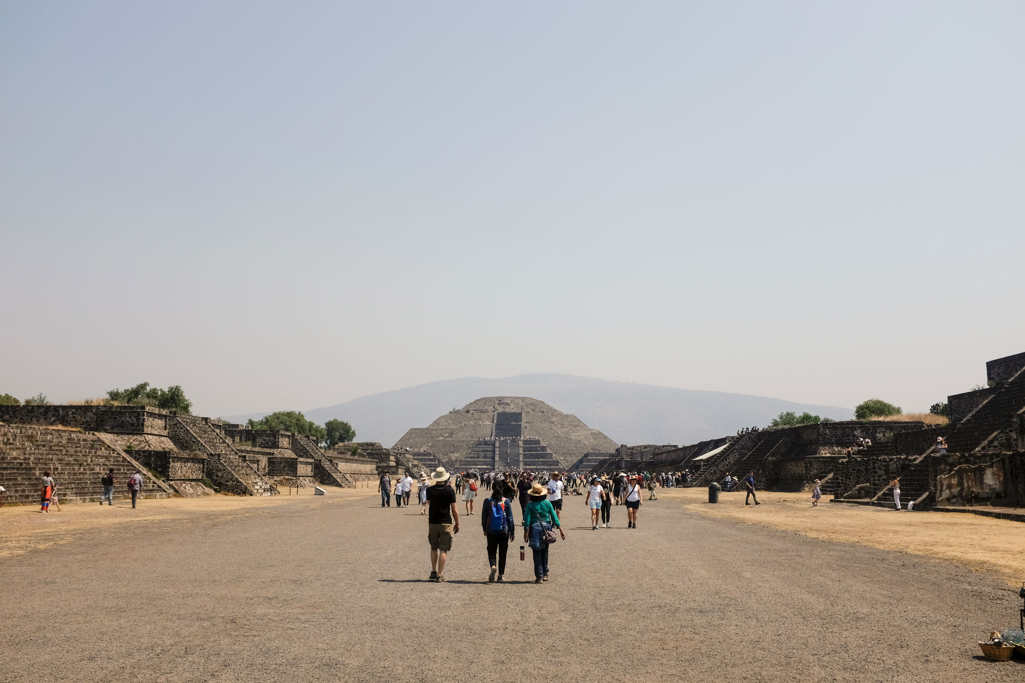 people walking on the avenue of the dead with the pyramid of the moon in the background