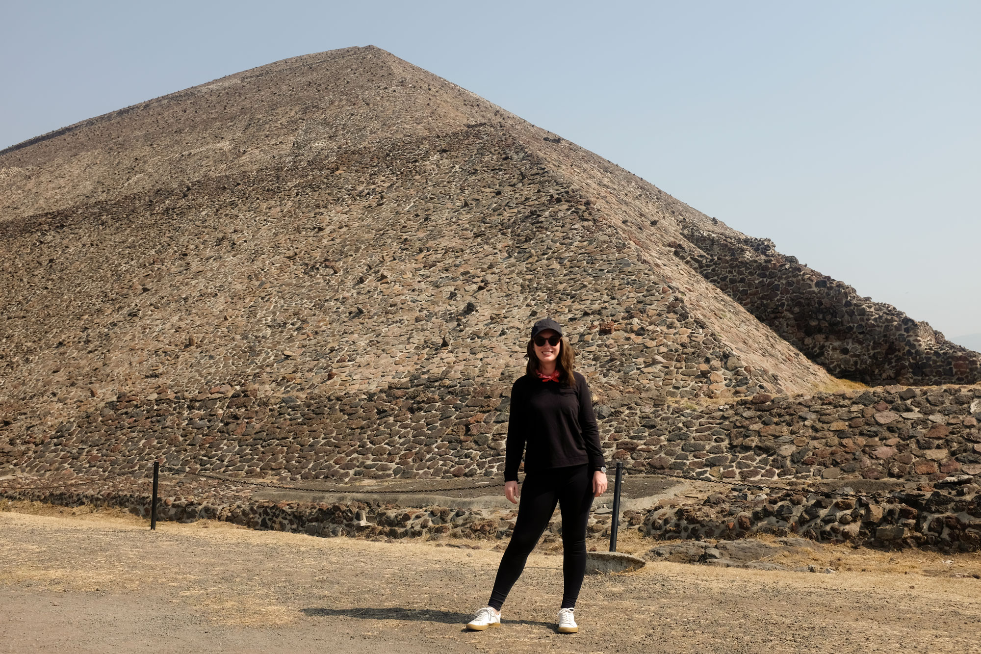 Alyssa standing in front of the pyramid of the sun in a black hat, sweatshirt, and leggings with a red bandana and white sneakers