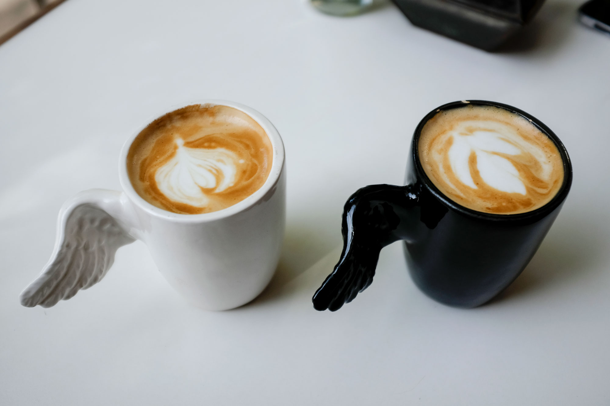 Two cappuccinos in mugs with angel wing shaped handles