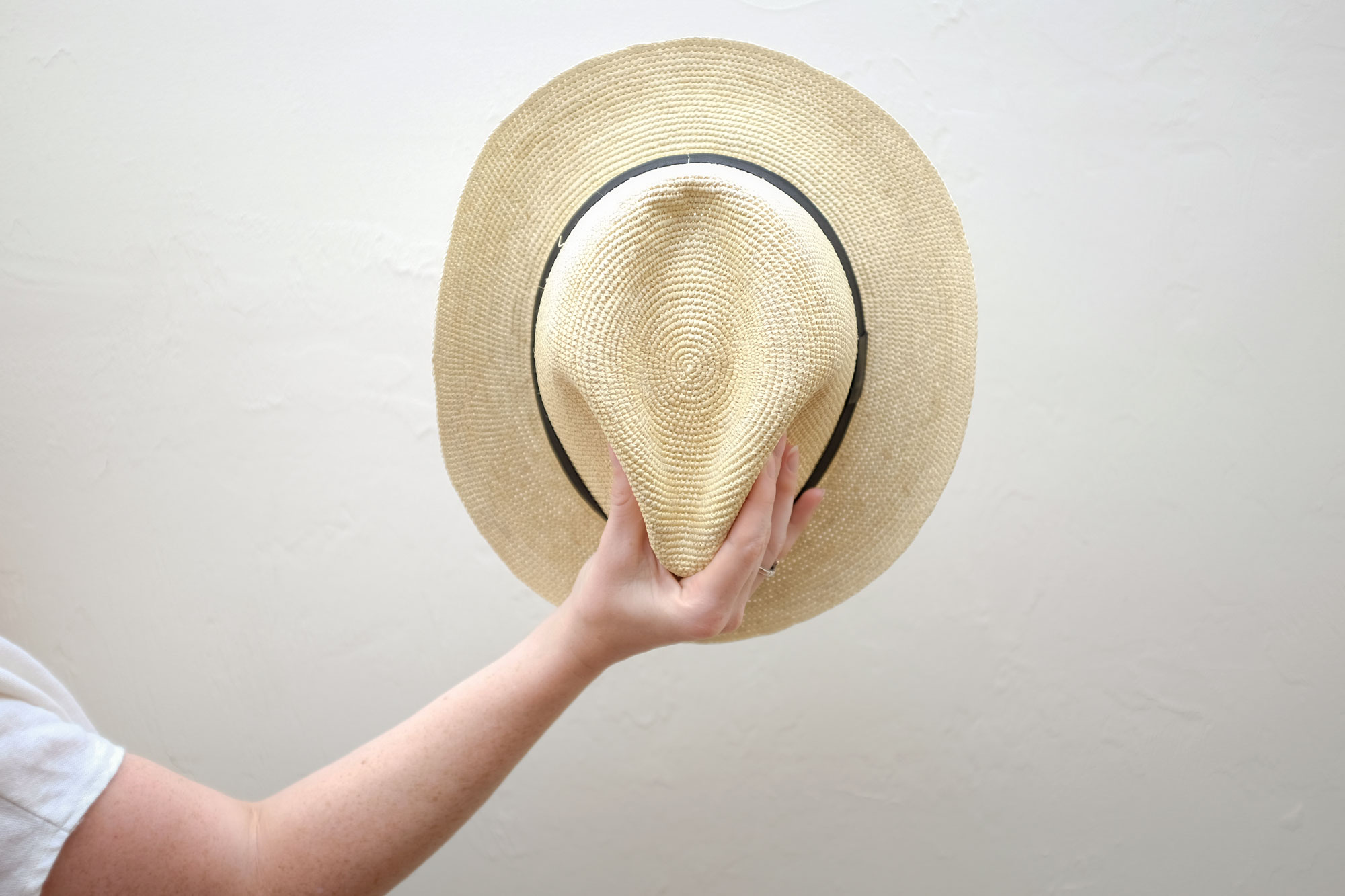 Alyssa pinching the crown of the Cuyana hat and holding it against the wall