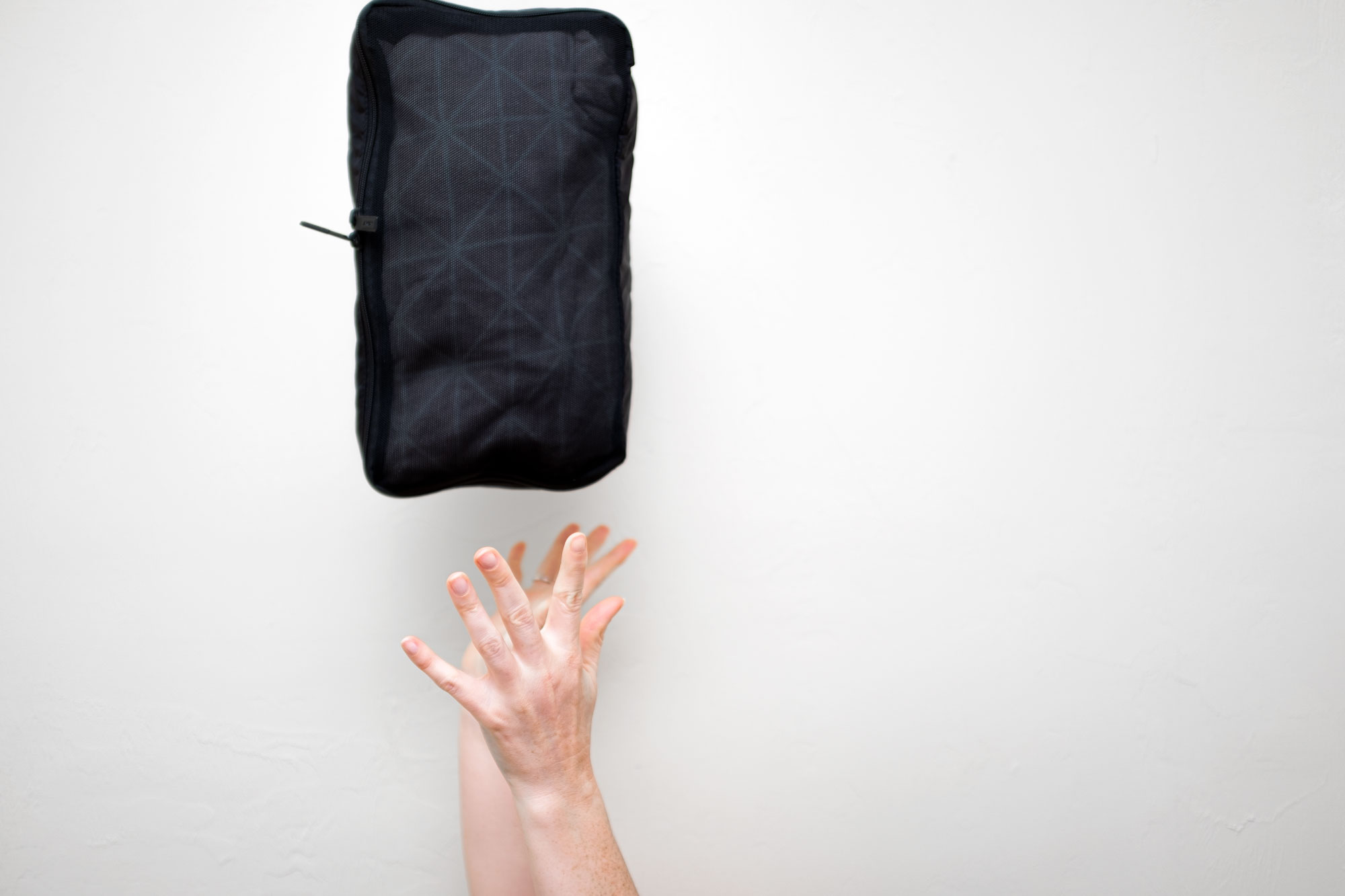 Alyssa throwing one of the packing cubes in the air - only her hands and the packing cube are in the frame