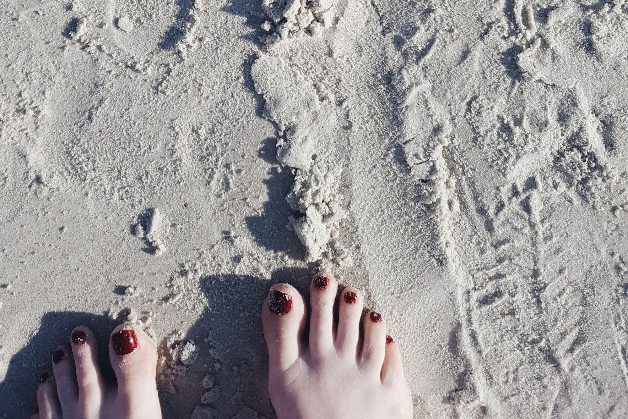 Sandy toes with red polish on the beach