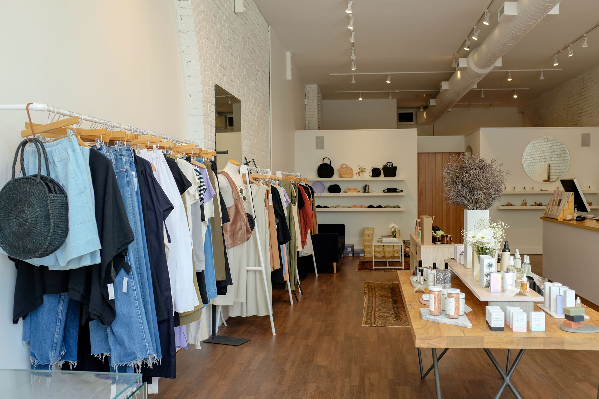 Interior view of shop with clothing lining the left wall and jewelry and skin care items on a table on the right