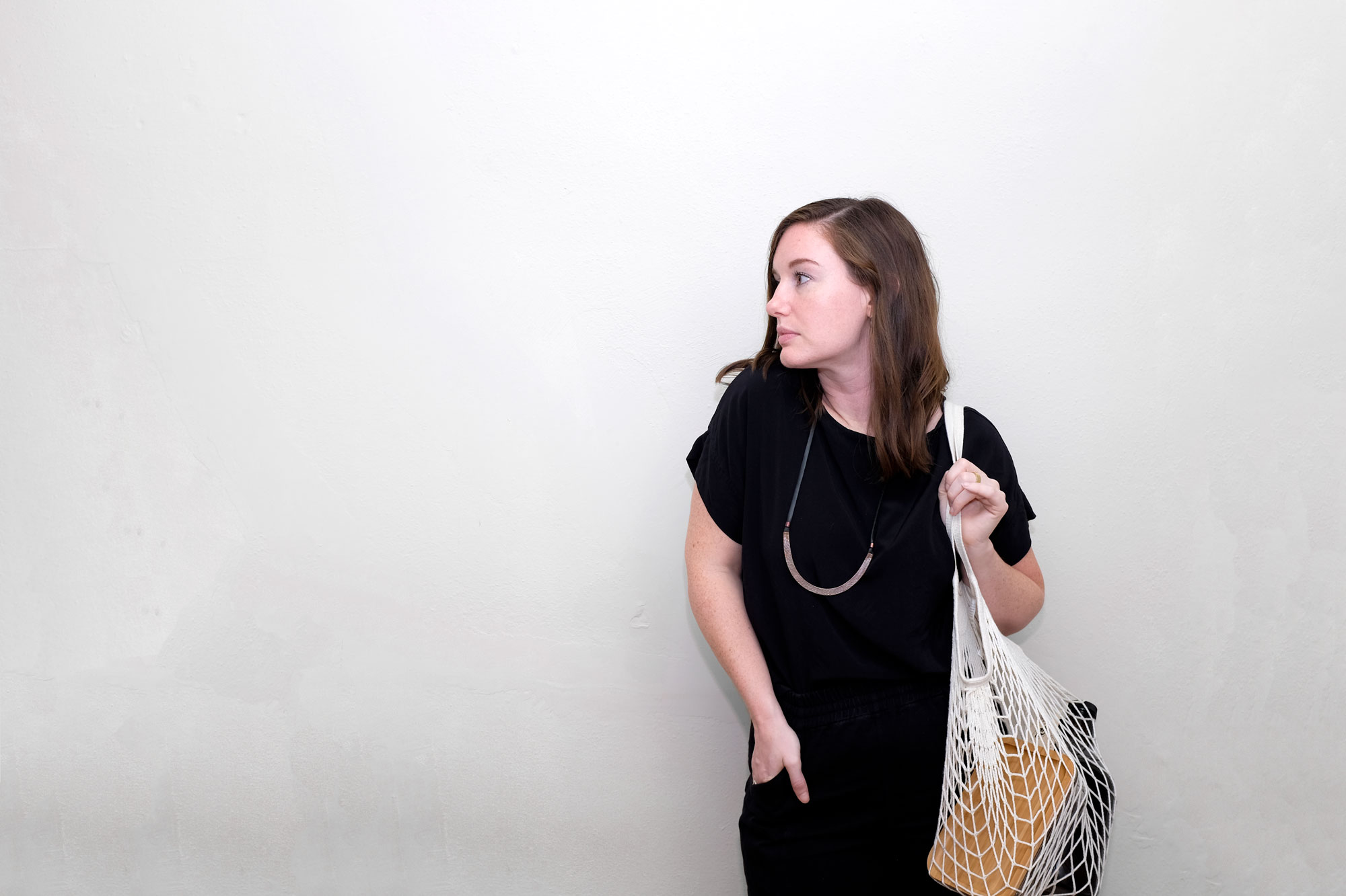 Alyssa standing with her hand in one pocket and a net bag slung across her other shoulder. Inside it are a glass container and growler