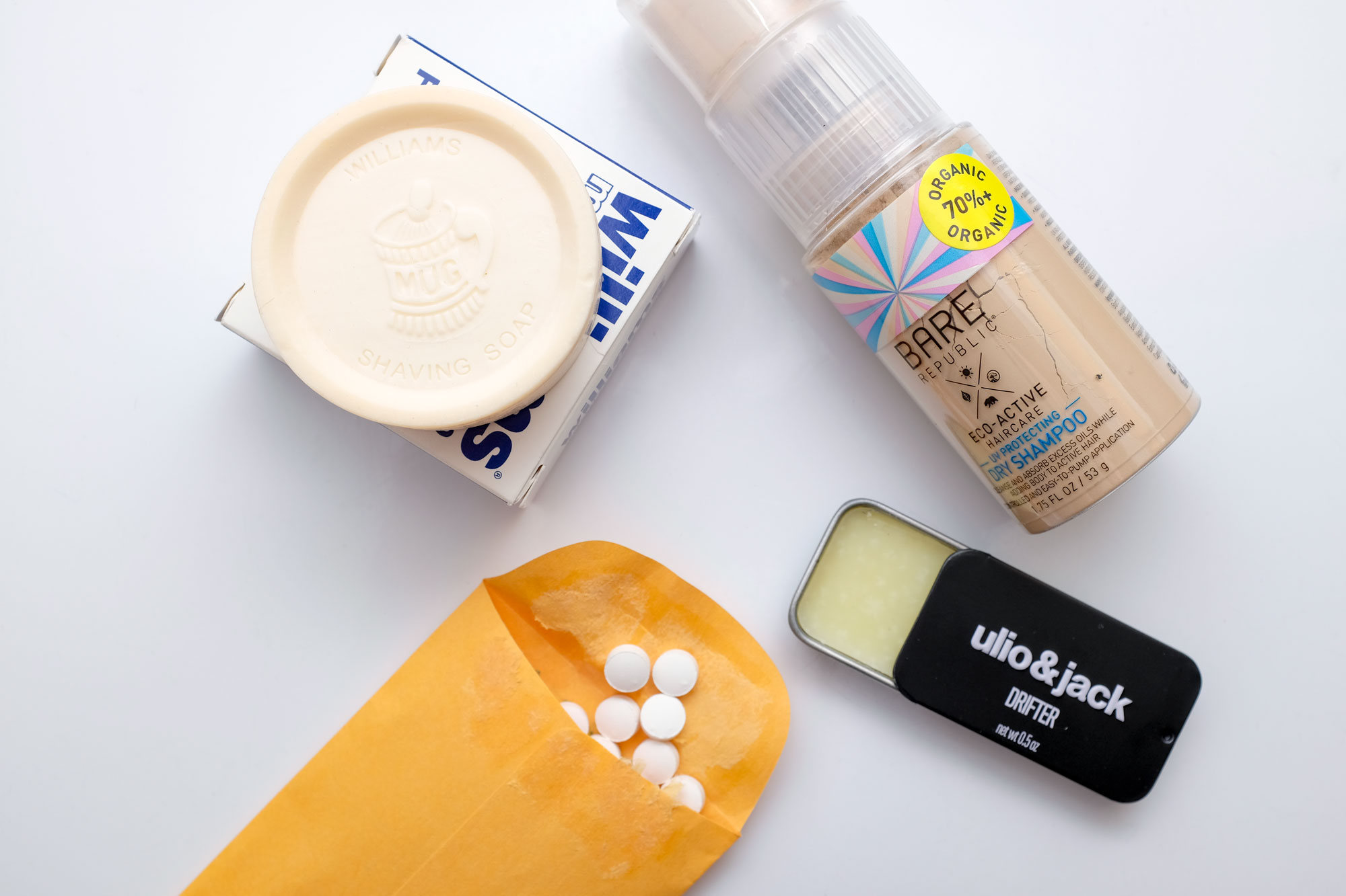 Flatlay with shave soap, powder dry shampoo, toothpaste tabs, and solid cologne