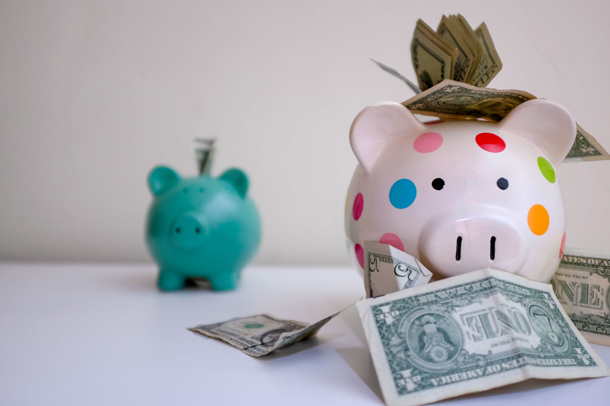 The two piggy banks, but this time the one with a lot of money is in the foreground and the piggy bank with less money is in the background.