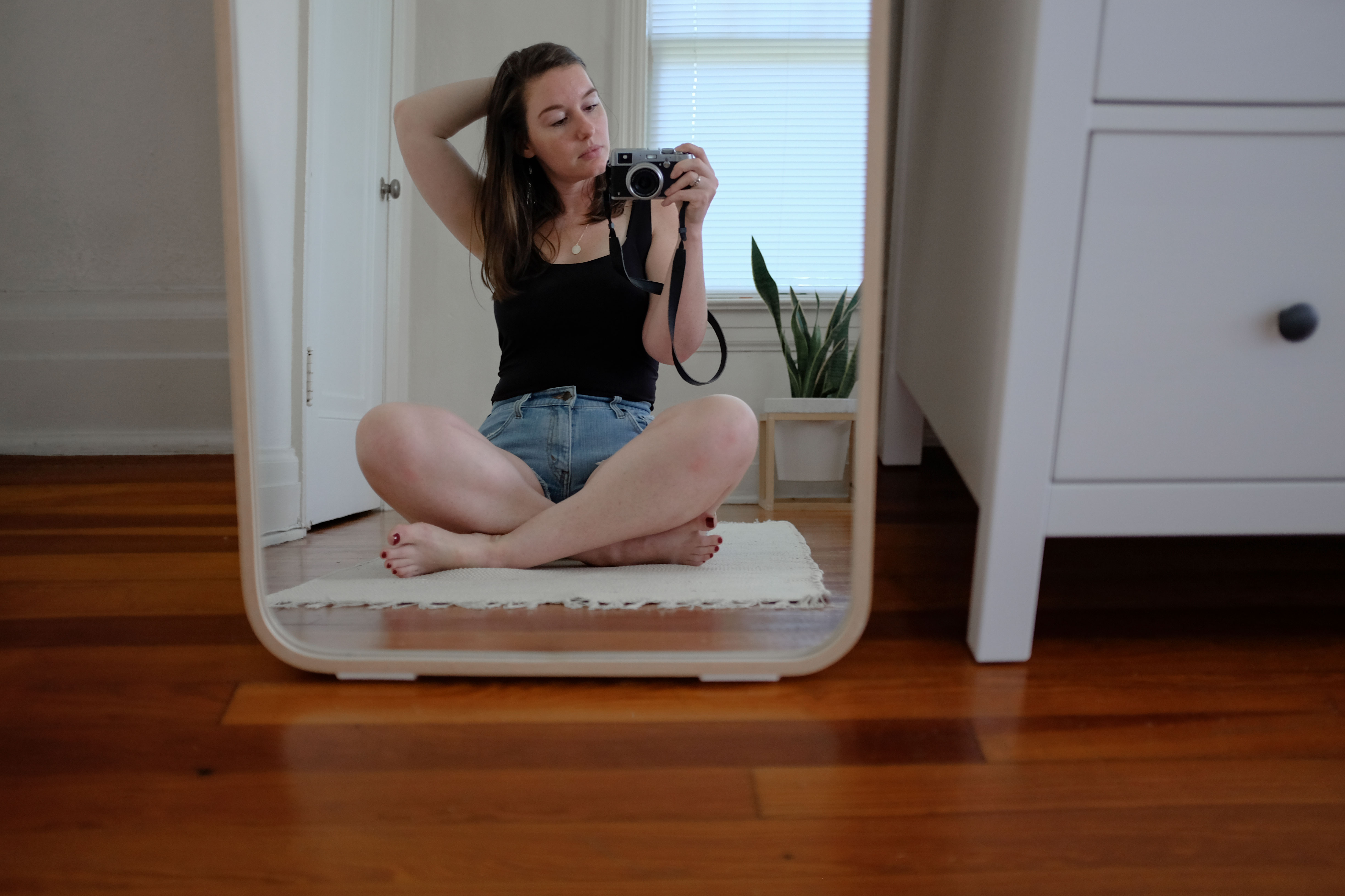 Krystal sitting cross-legged in front of a mirror in a black tank and jean shorts
