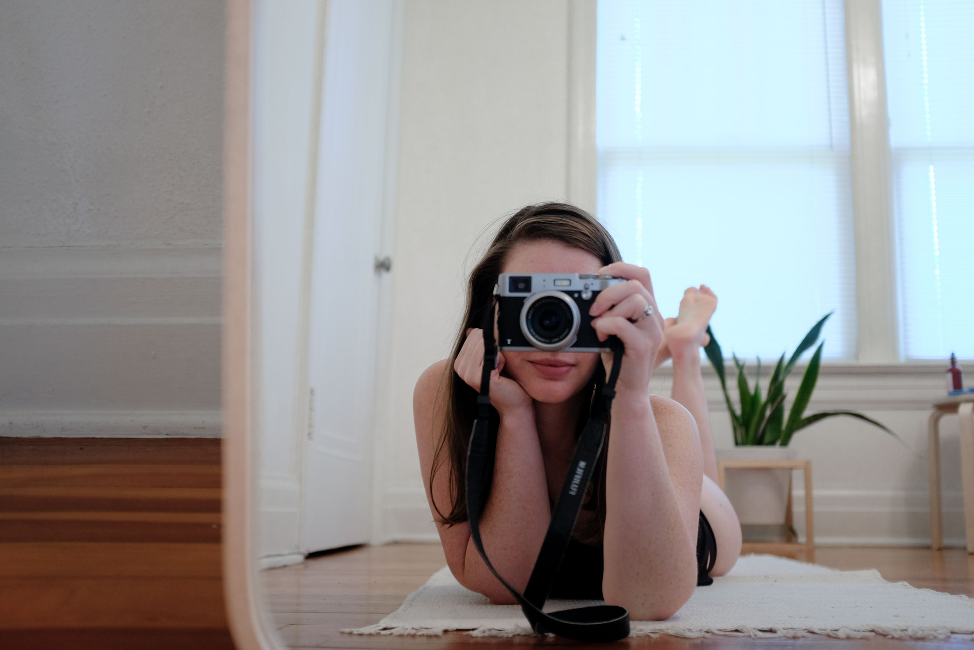 Krystal laying in front of a mirror holding a camera. She is wearing a black tank and underwear