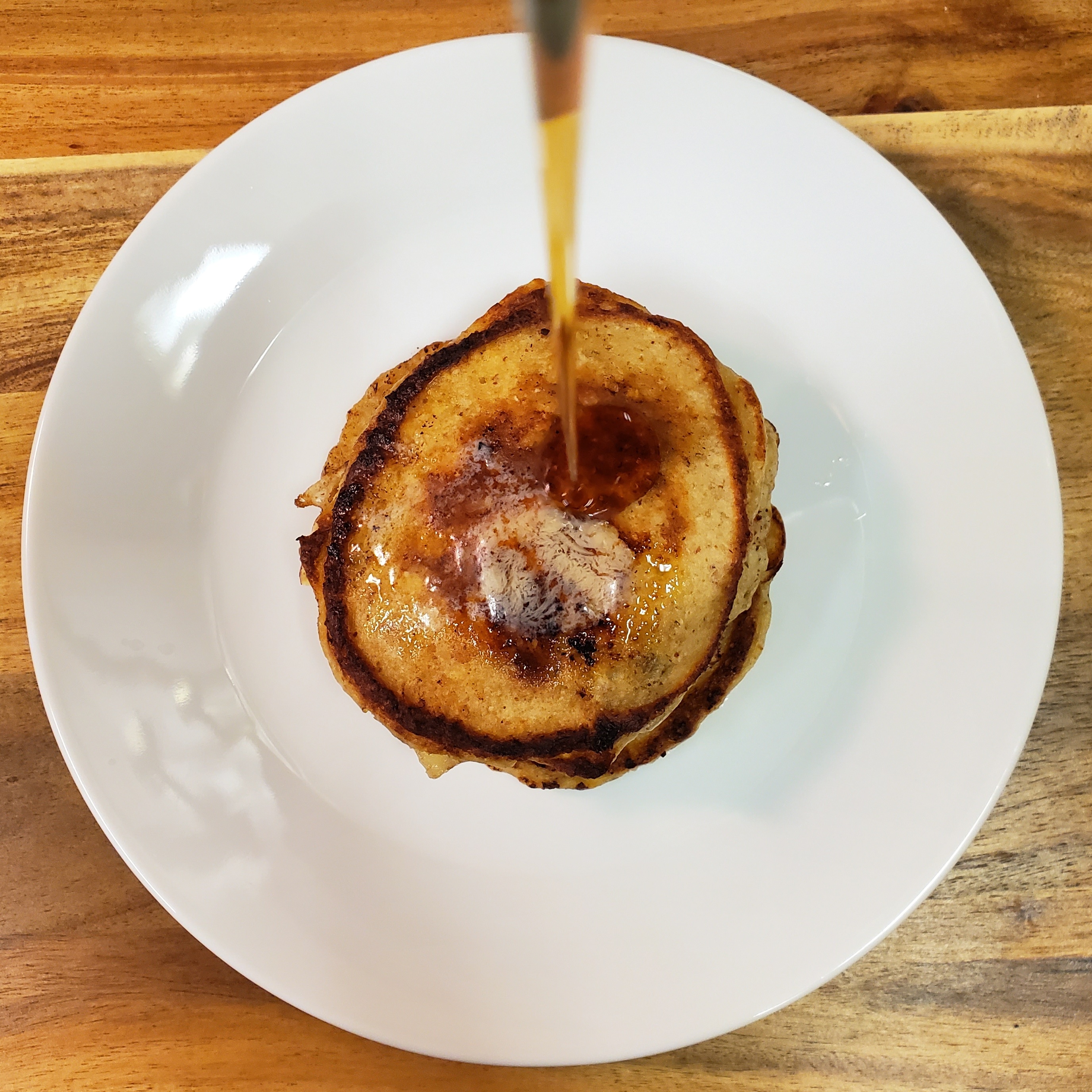 Mini stack of pancakes on a white plate, maple syrup is pouring down in a stream