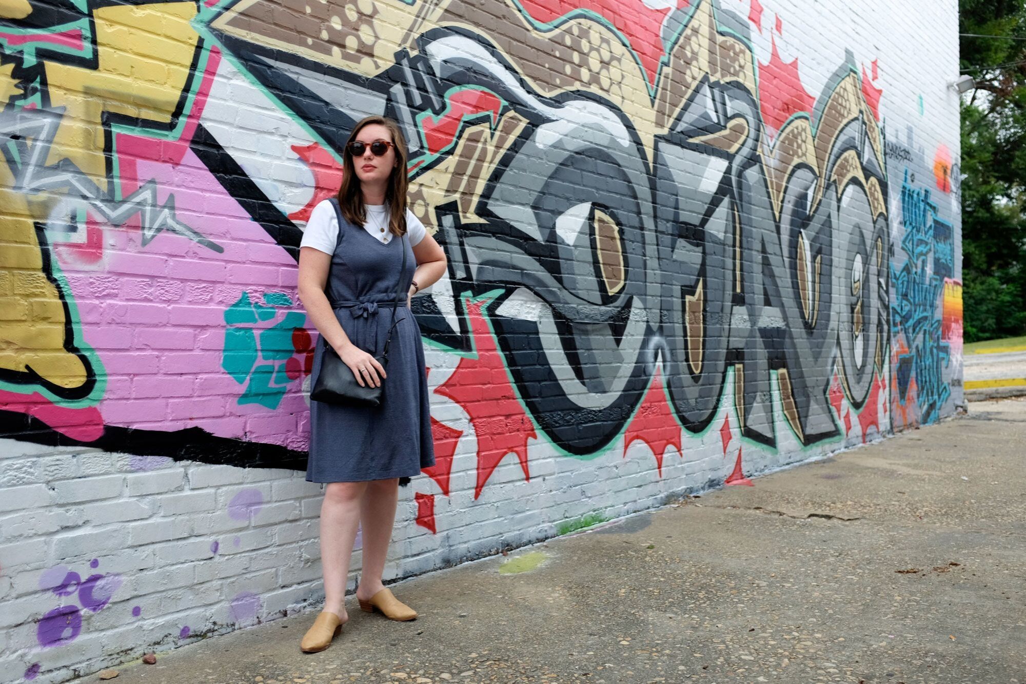 Alyssa standing in front of a graffiti wall in a blue dress with a white tee underneath